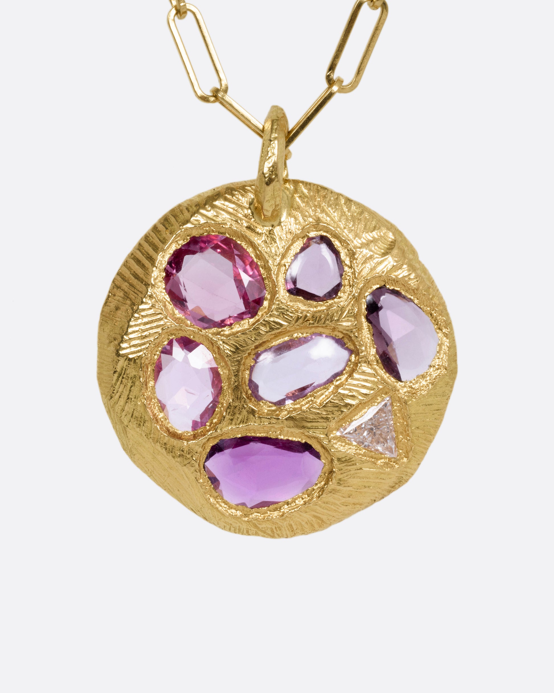 A yellow gold necklace with a circular pendant with pink sapphires and one trillion cut diamond, shown from the front.