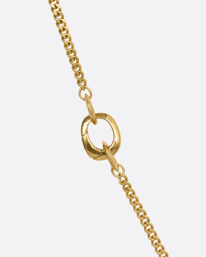 A close up of a yellow gold cable chain with an asymmetrical side bail.