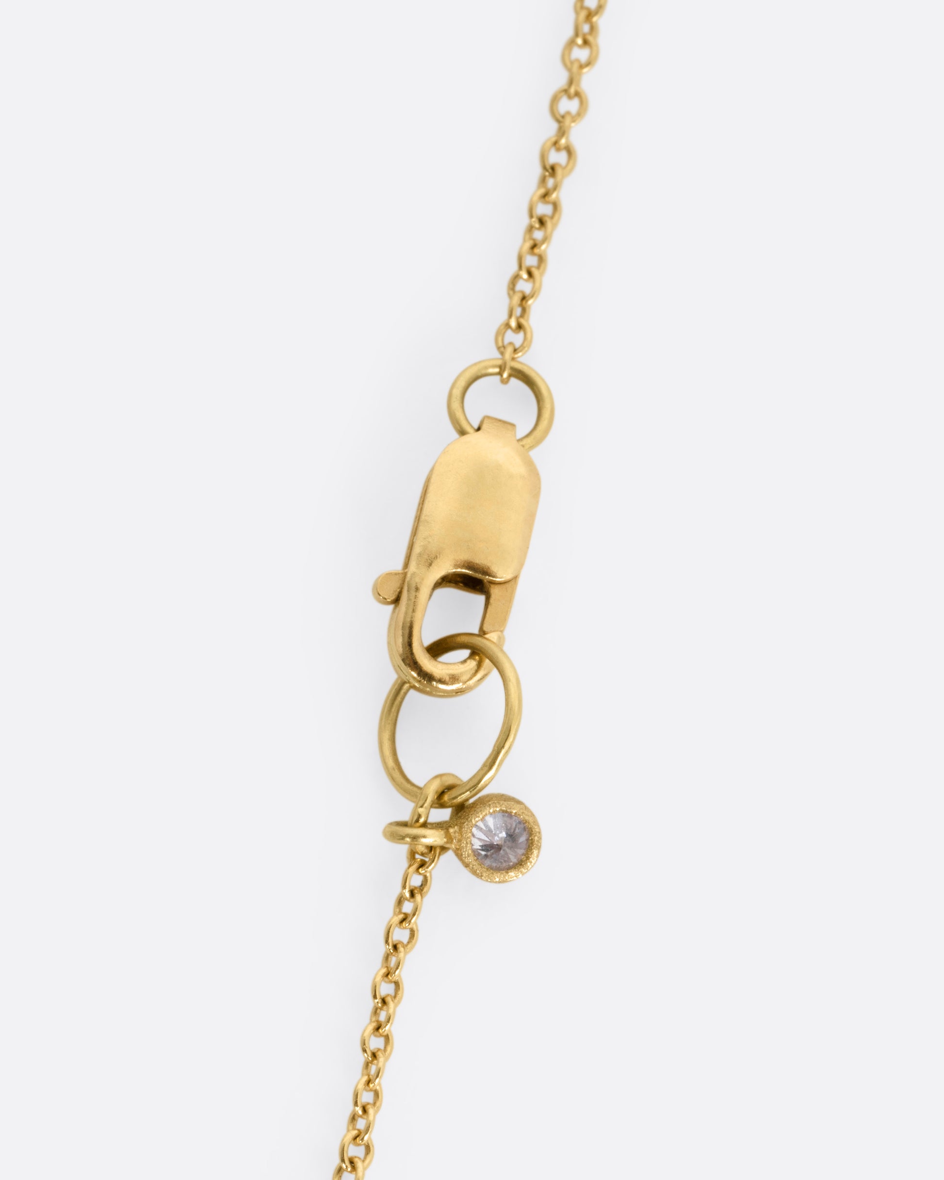 A close up of a yellow gold clasp with a diamond dangle.