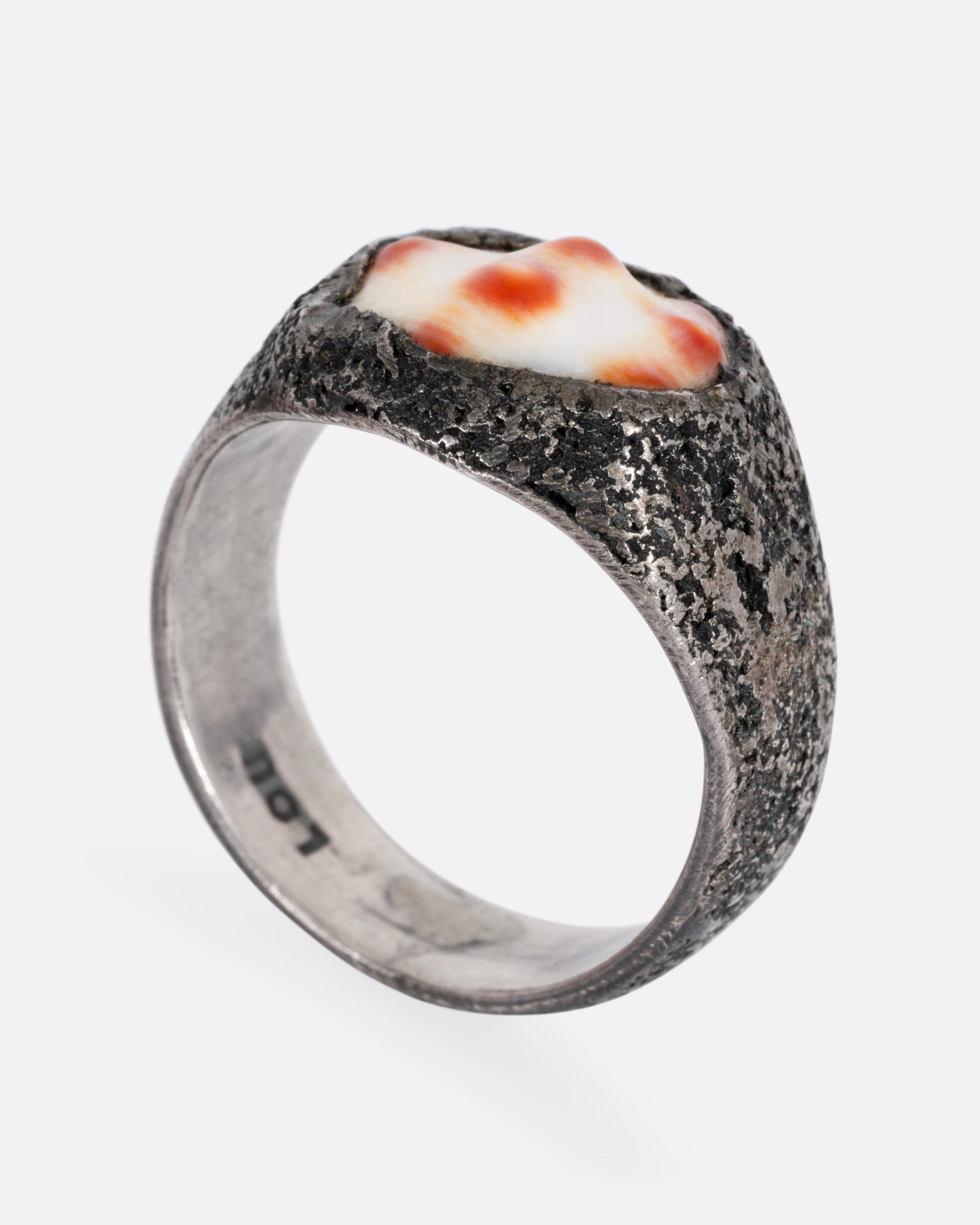 A silver signet ring with a speckled shell, shown from the side standing up.