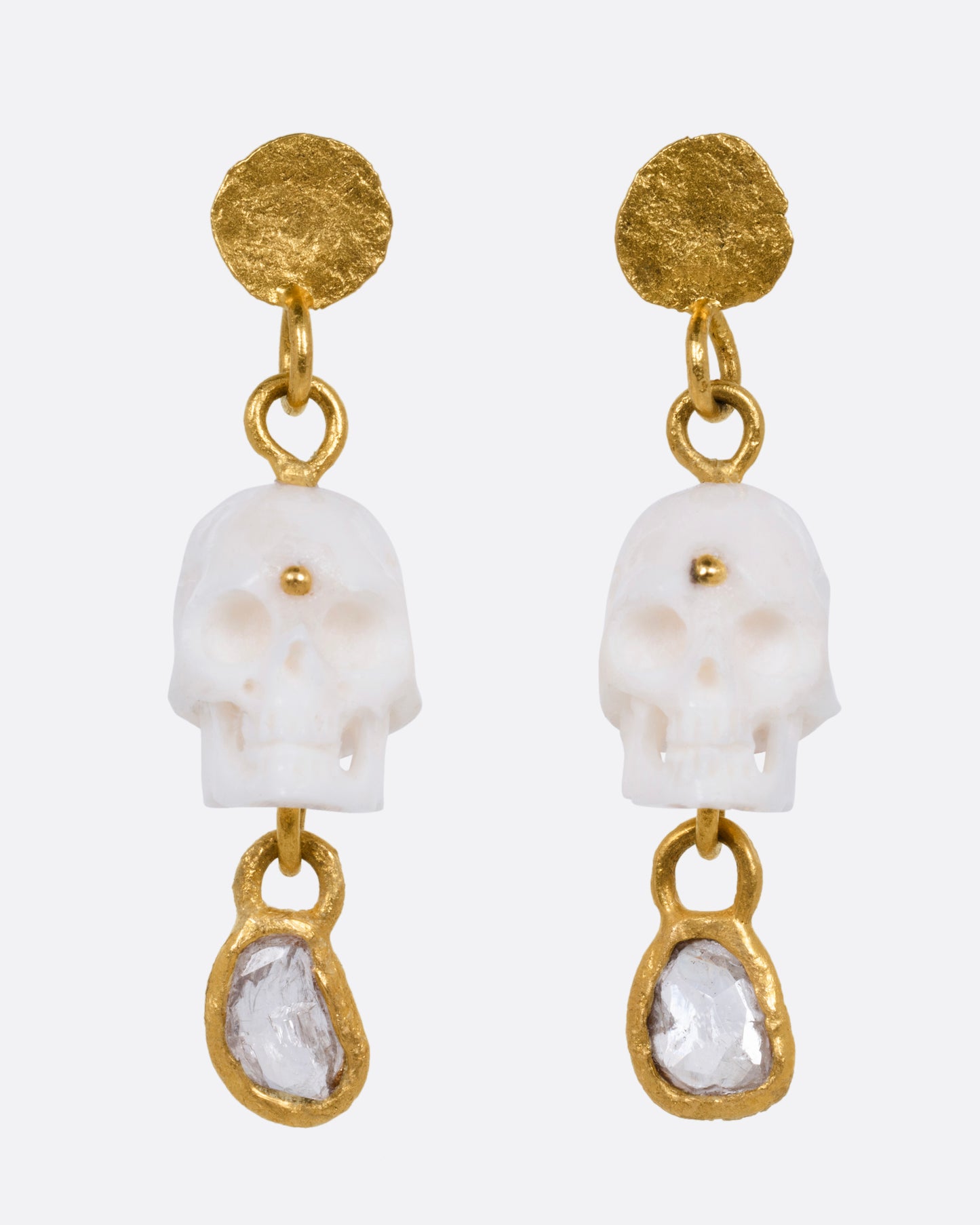 A pair of yellow gold drop stud earrings with carved bone skulls and Borneo diamonds, shown from the front.
