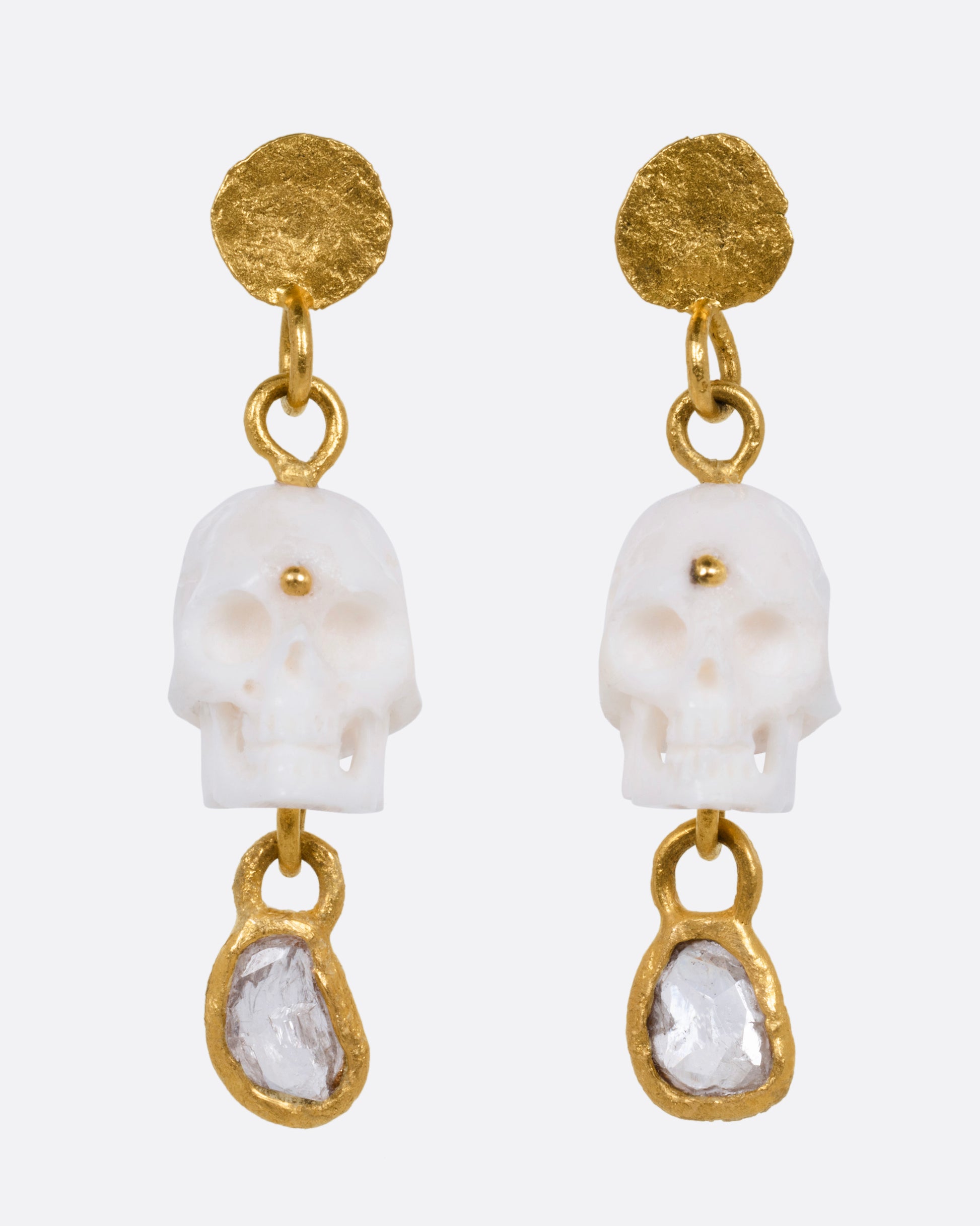 A pair of yellow gold drop stud earrings with carved bone skulls and Borneo diamonds, shown from the front.