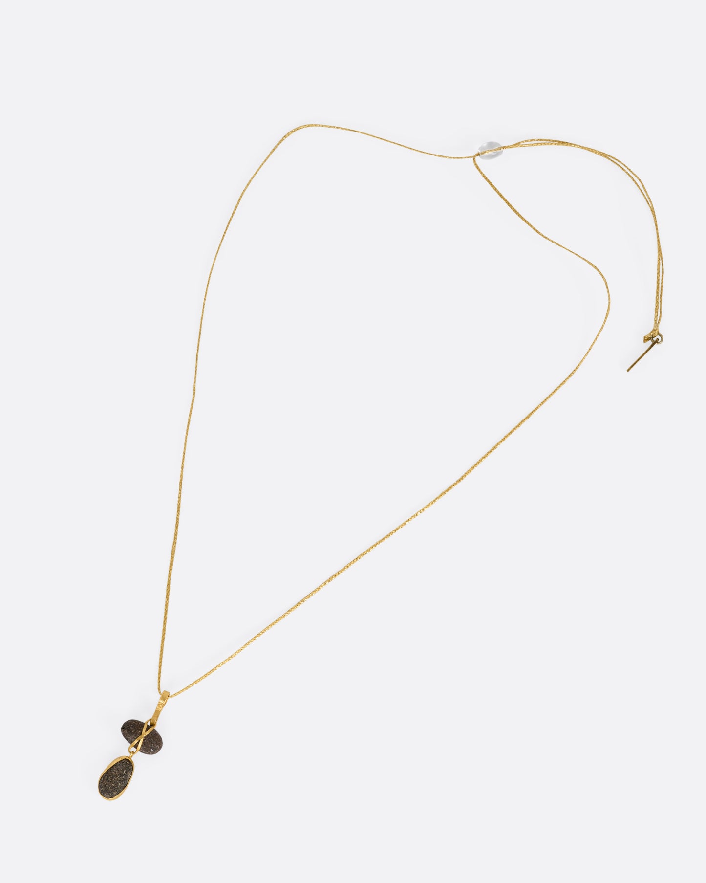 A yellow gold pendant with two Japanese river pebbles on a cord, shown from the front.