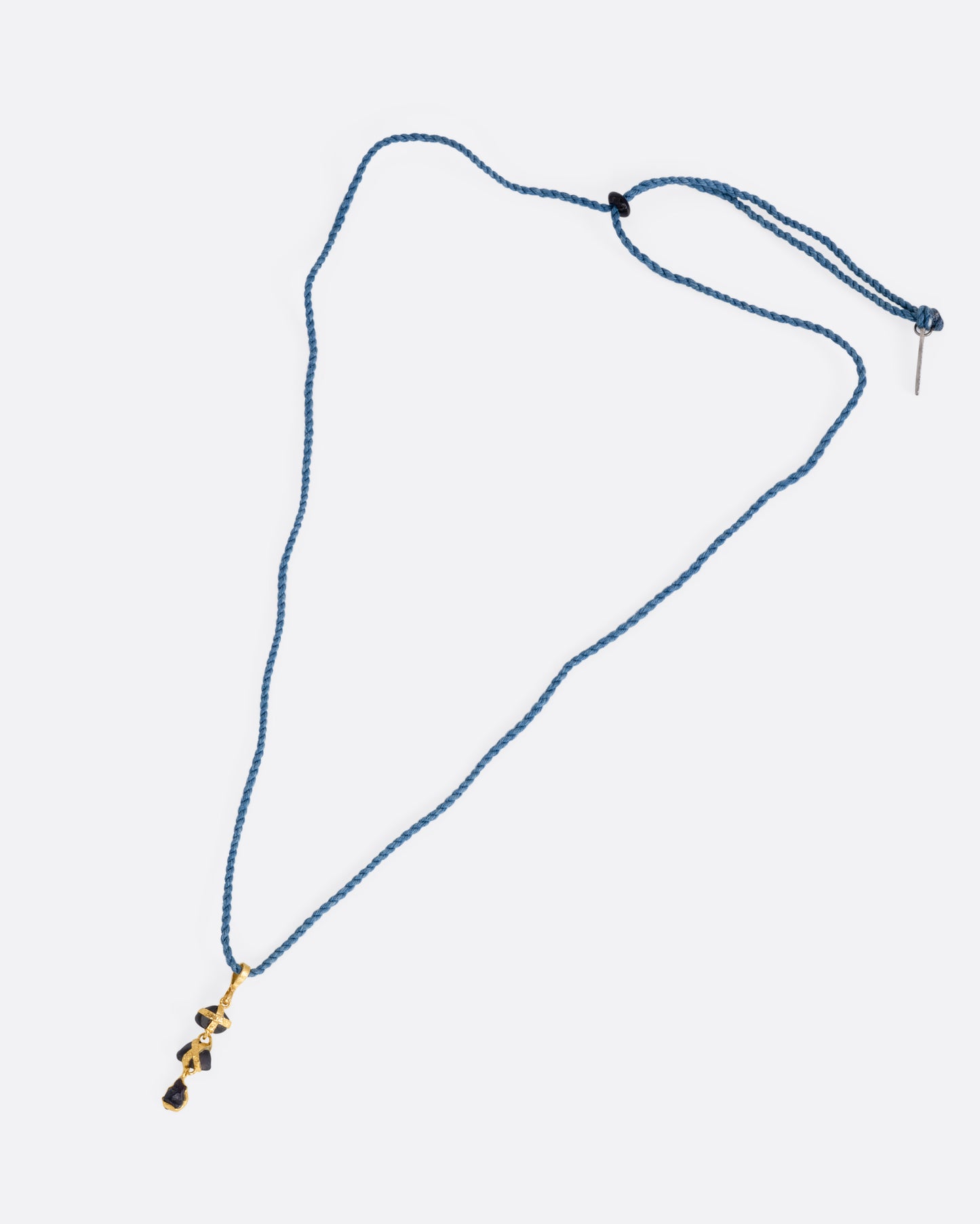 A yellow gold pendant with three  raw sapphires on a cord, shown from the front.