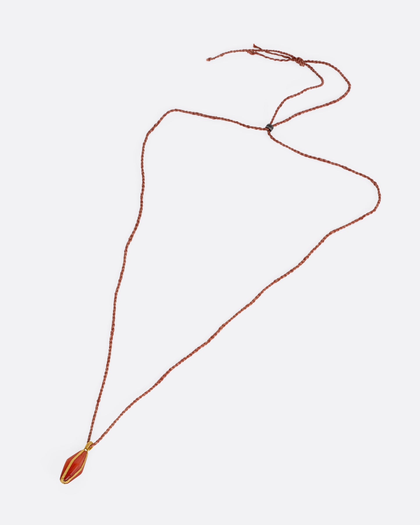 A carnelian pendant wrapped in yellow gold and suspended from a cord, shown from the front lying flat. 
