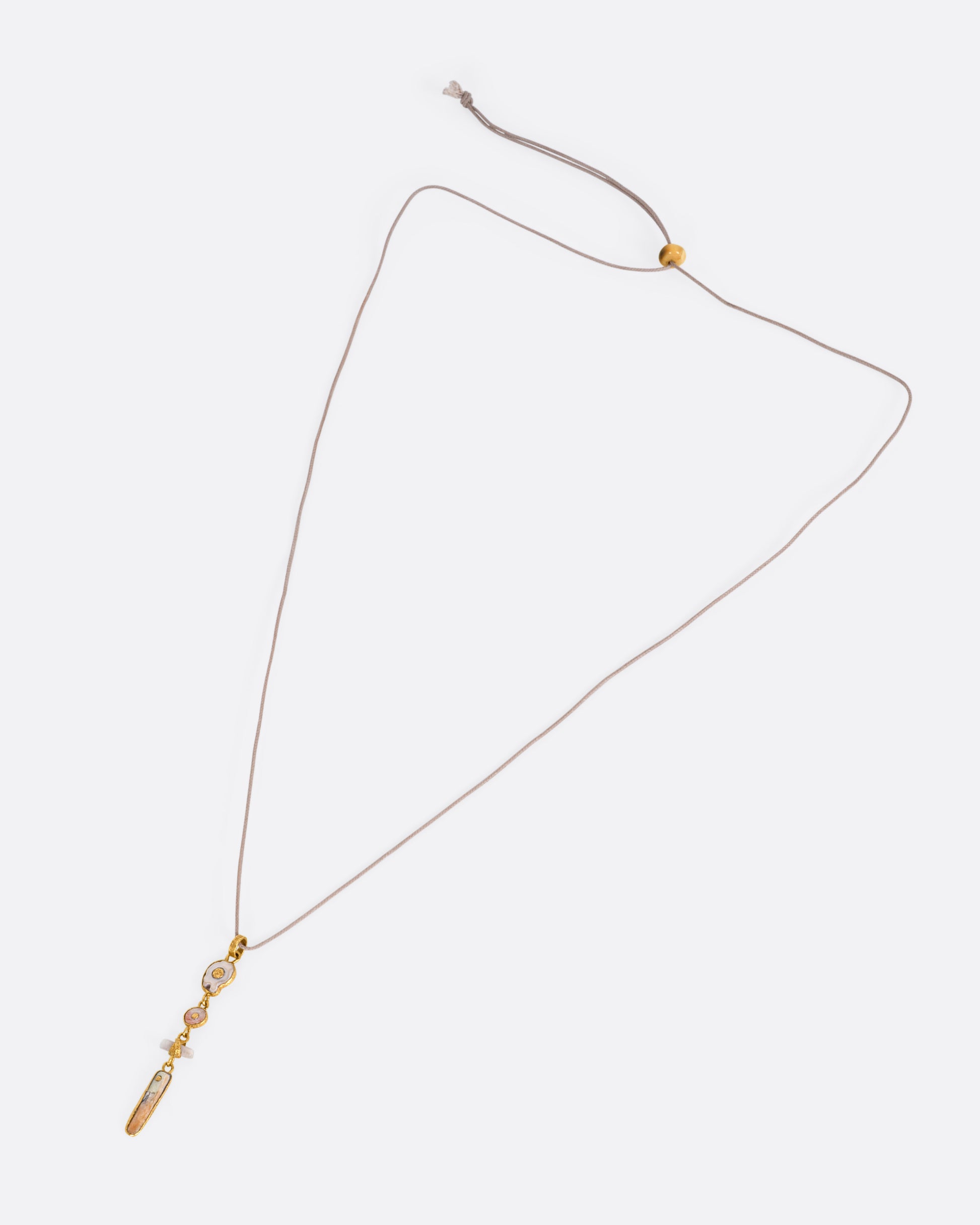 A yellow gold pendant with four gold wrapped pieces on a cord, shown from the front.