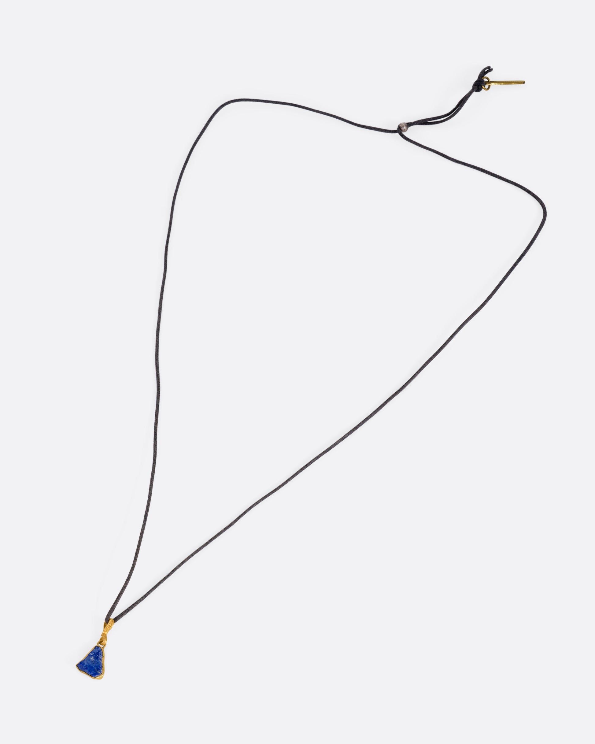 A yellow gold pendant with a raw triangular lapis on a black cord, shown from the front.