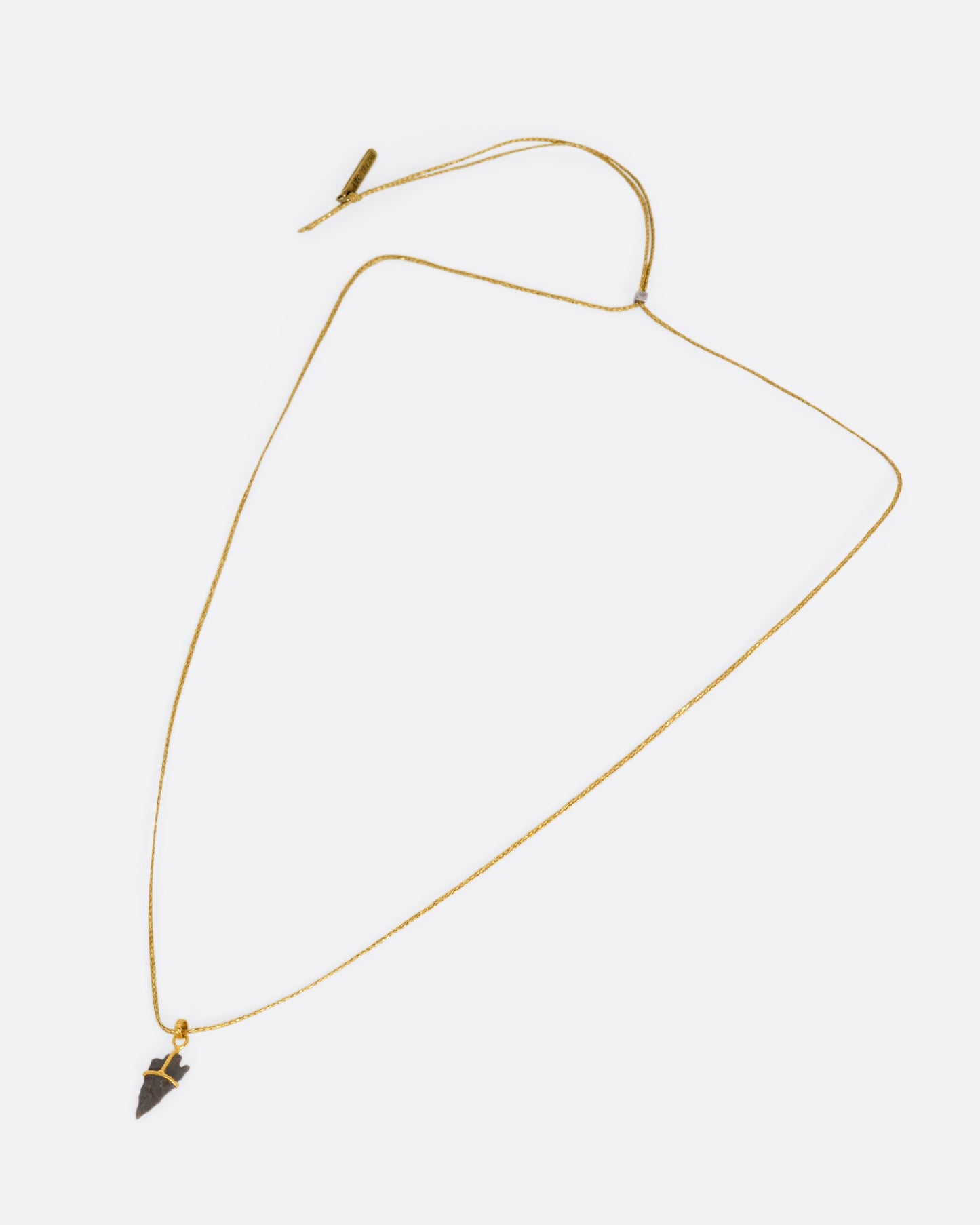 A yellow gold pendant with an ancient arrowhead on a cord, shown from the front.