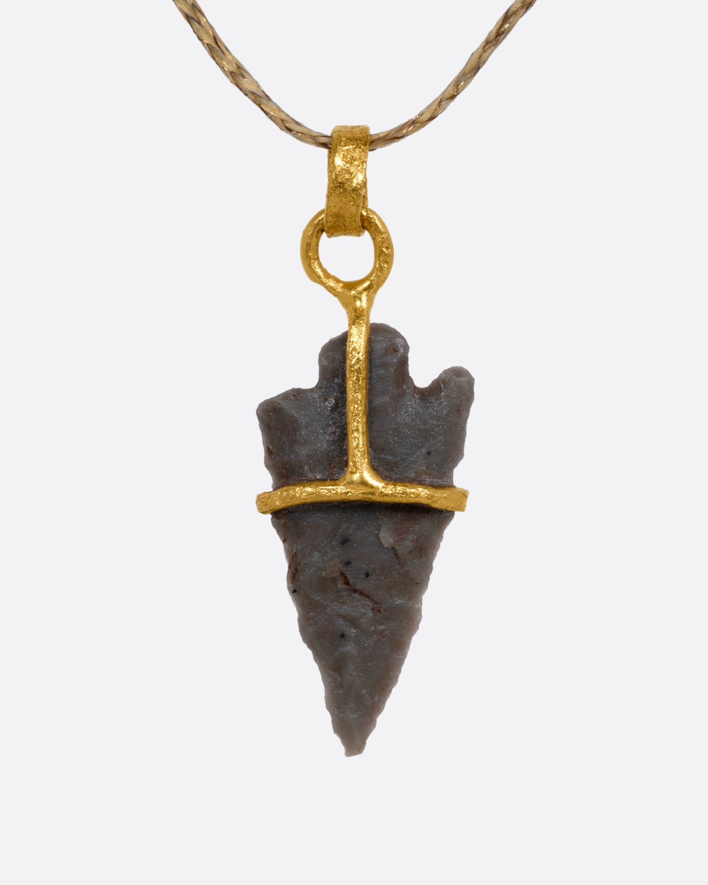 A yellow gold pendant with an ancient arrowhead on a cord, shown from the front.