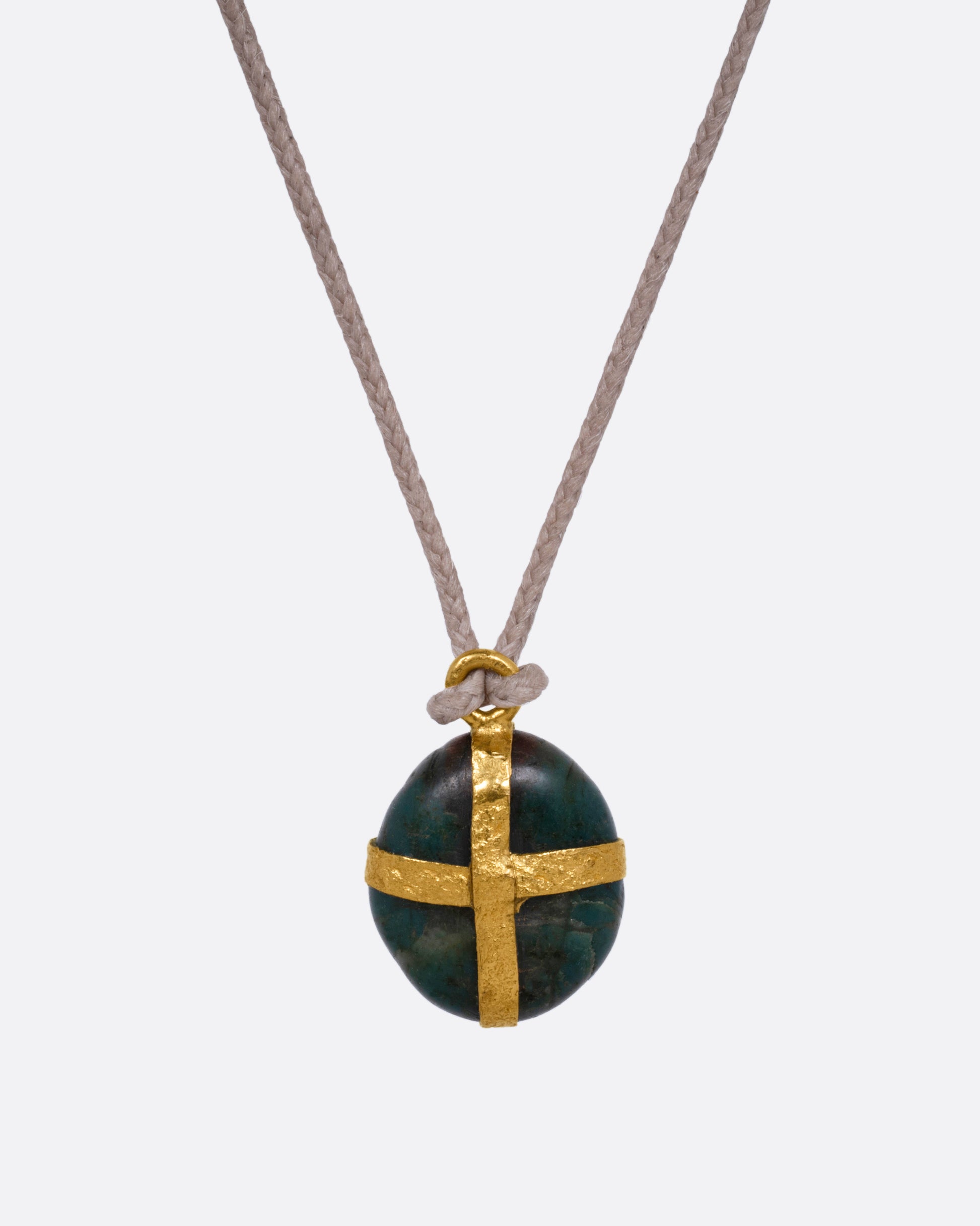 A Japanese river pebble pendant wrapped in yellow gold and hanging from a cord, shown from the front.