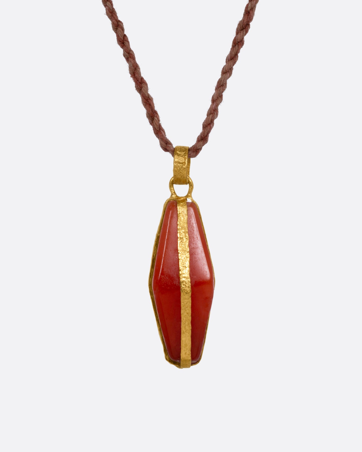 A carnelian pendant wrapped in yellow gold and suspended from a cord, shown from the front. 