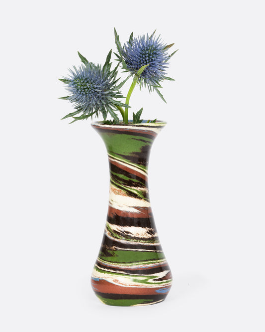A green, brown, and white swirled bud vase. Shown with blue flowers. 