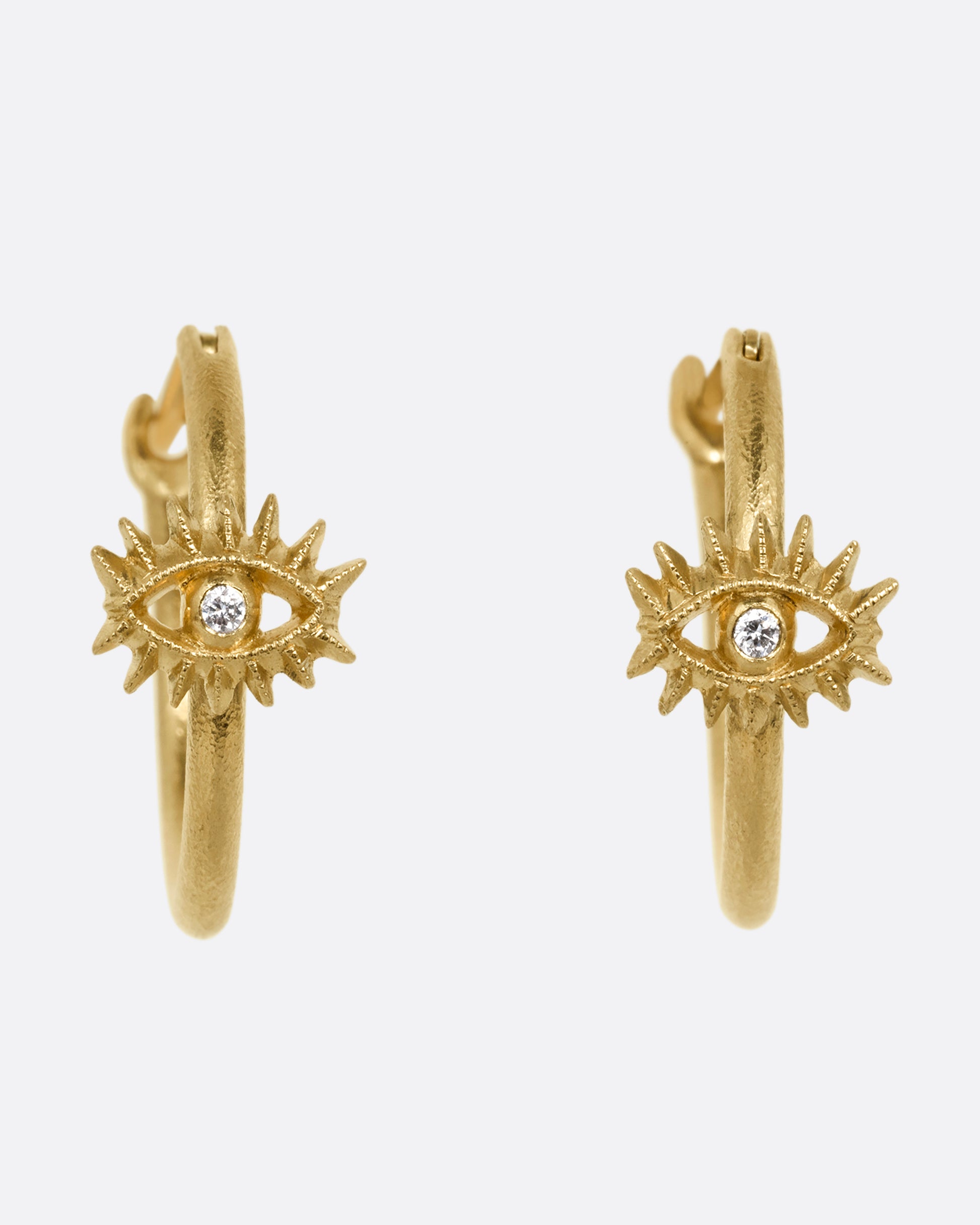 A pair of yellow gold hoop earrings with diamond studded eyes with dramatic lashes. Shown from the front.
