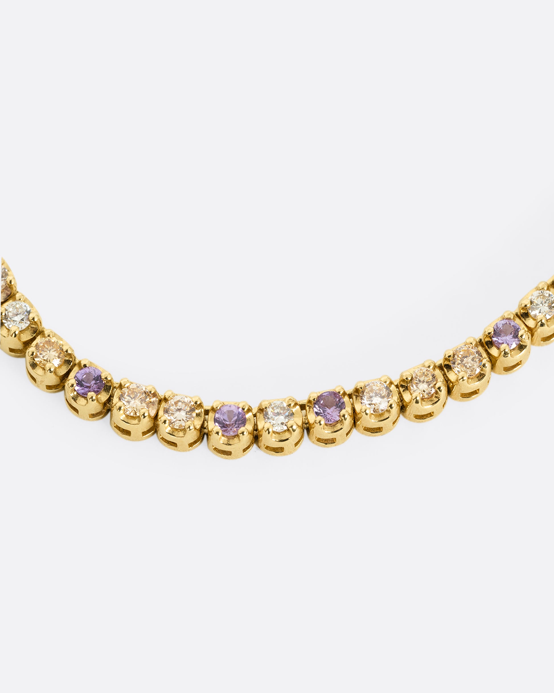 A close up of the center of a yellow gold cable chain necklace with peach and yellow diamonds and purple sapphires in a 'partial tennis' setting. Shown from the front.