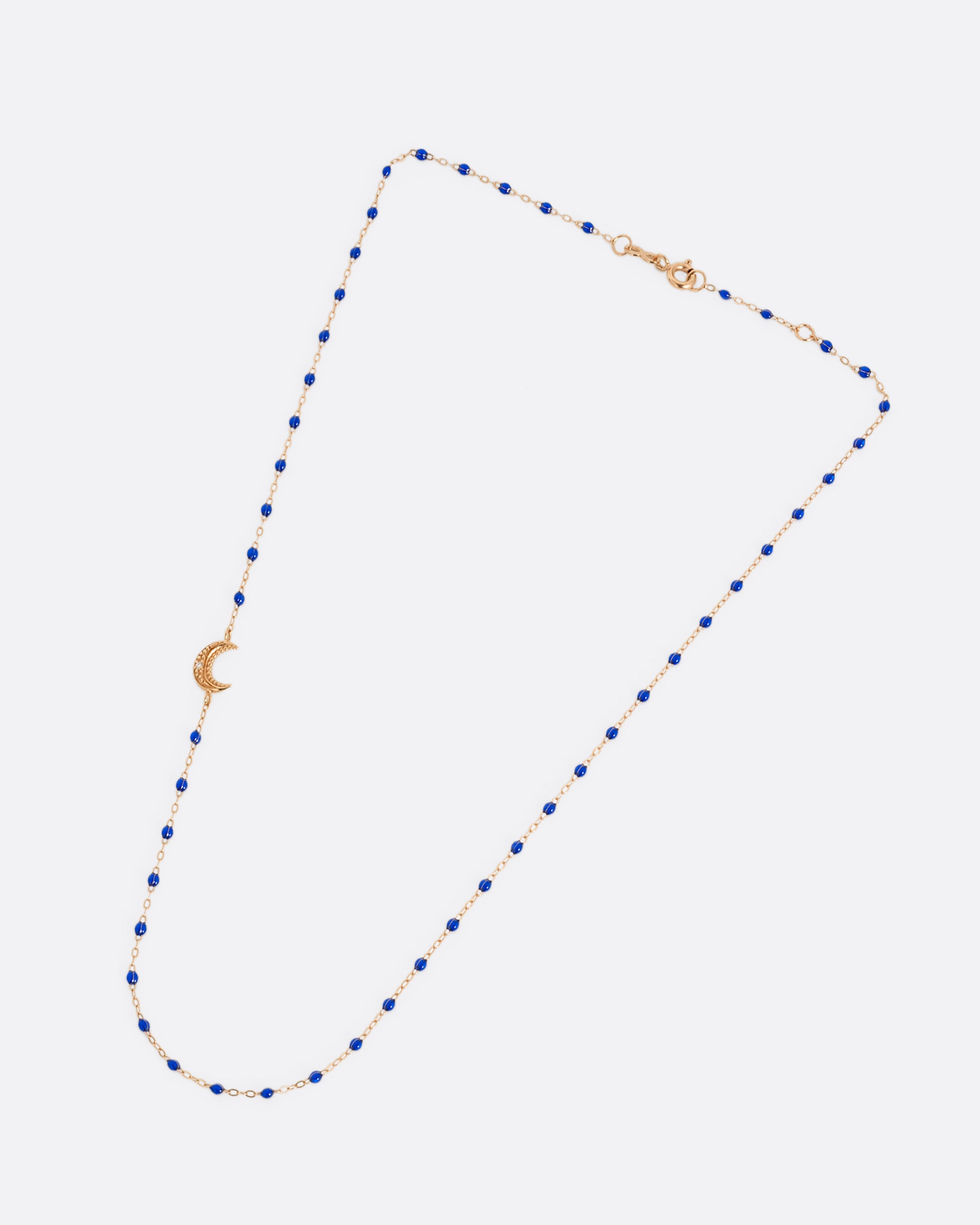 A rose gold cable chain necklace with lapis blue resin droplets along the chain and a crescent moon charm with a diamond on one side. Shown closed lying flat from the front.