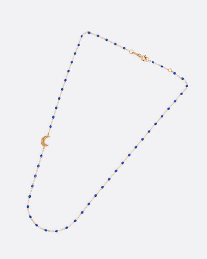 A rose gold cable chain necklace with lapis blue resin droplets along the chain and a crescent moon charm with a diamond on one side. Shown closed lying flat from the front.