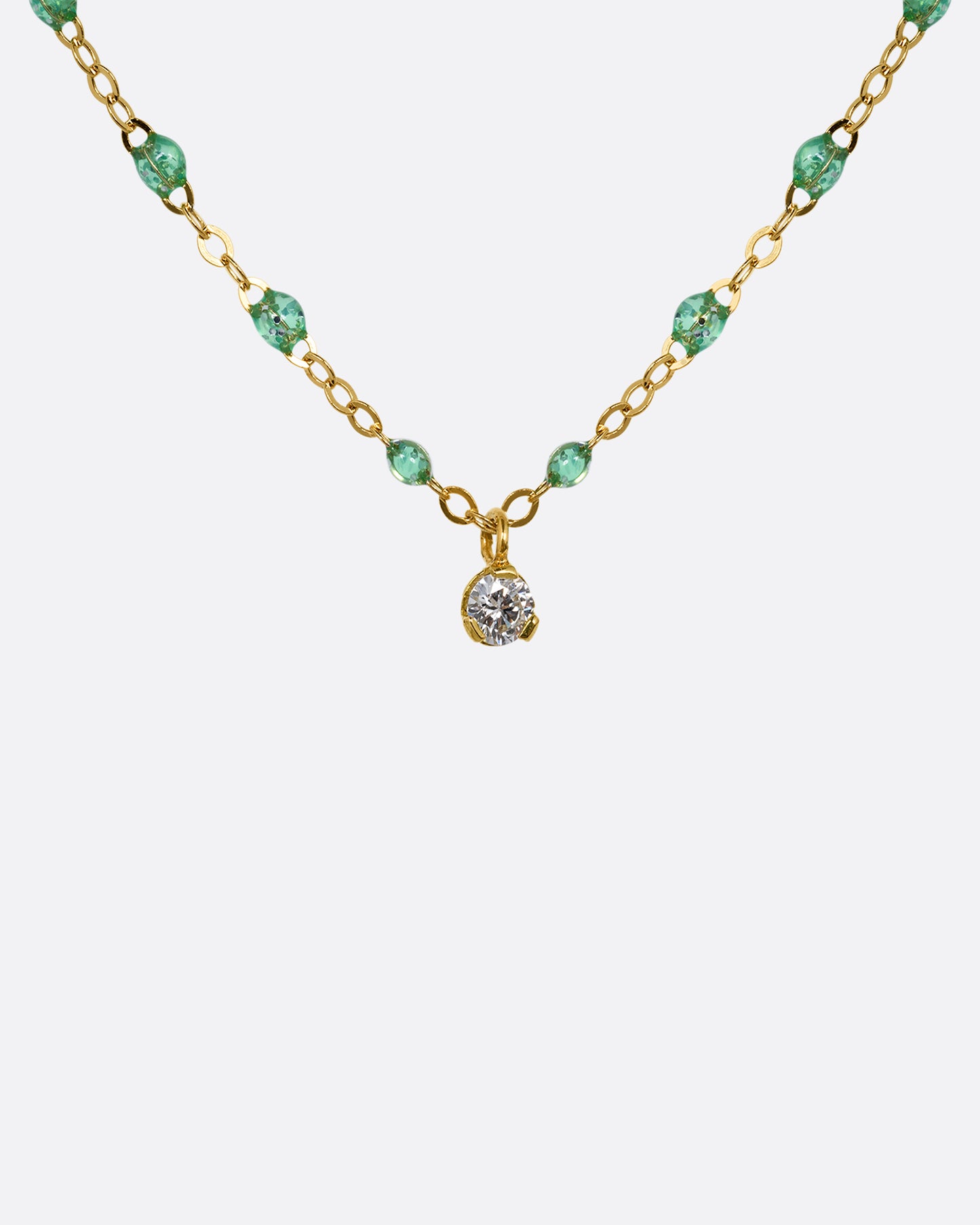 A close up of a yellow gold cable chain necklace with mint green resin droplets and a diamond charm at the center. Shown from the front.