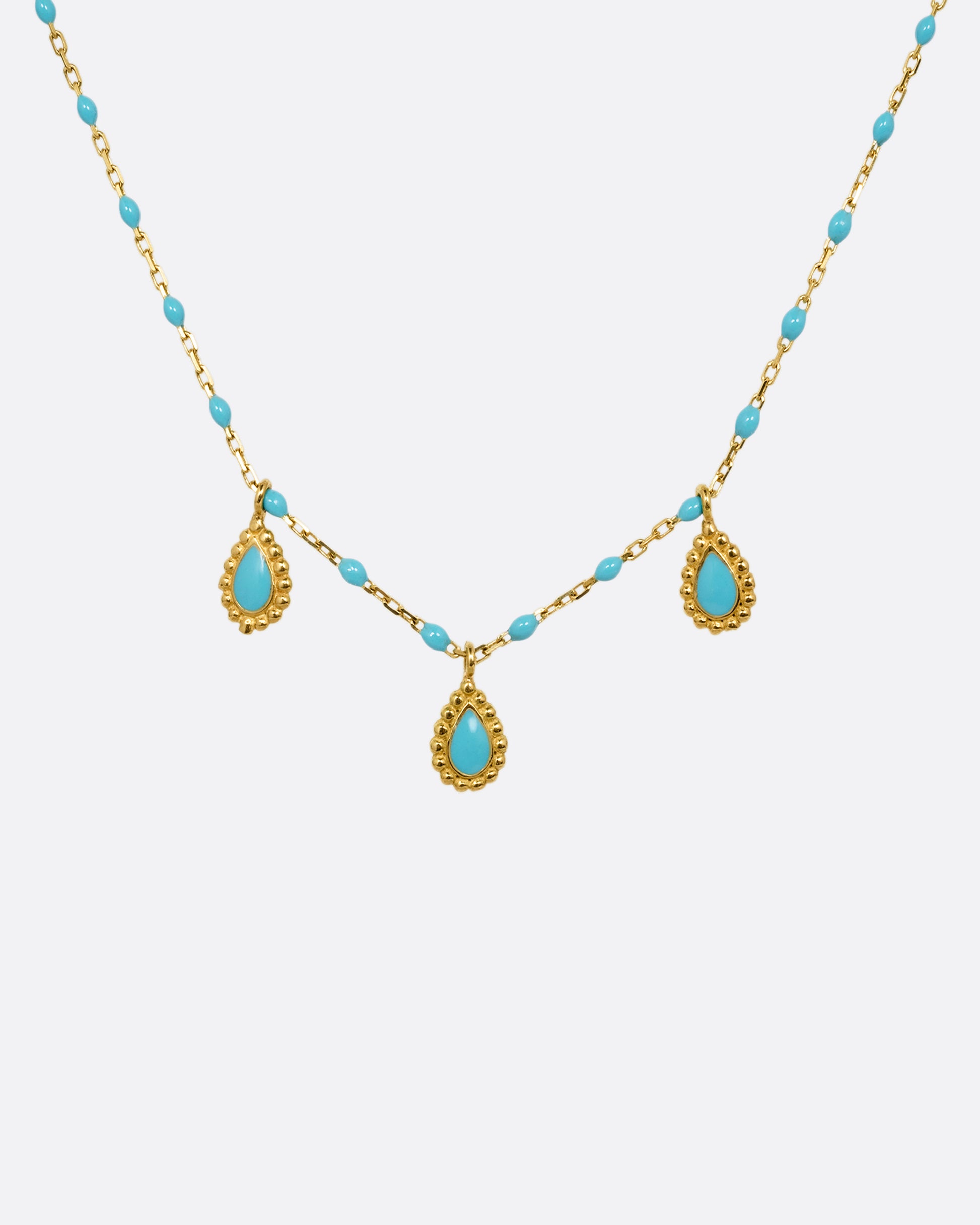 A yellow gold cable chain necklace with turquoise resin droplets along the chain and three teardrop shaped gold charms with turquoise resin centers. Shown from the front.