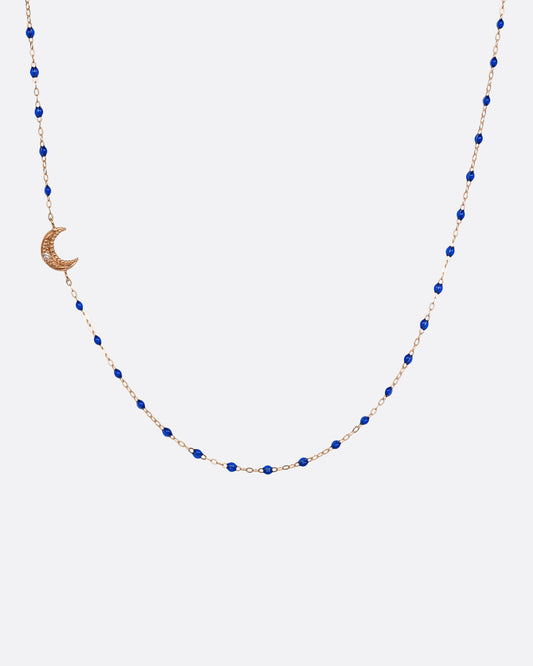 A rose gold cable chain necklace with lapis blue resin droplets along the chain and a crescent moon charm with a diamond on one side. Shown from the front.