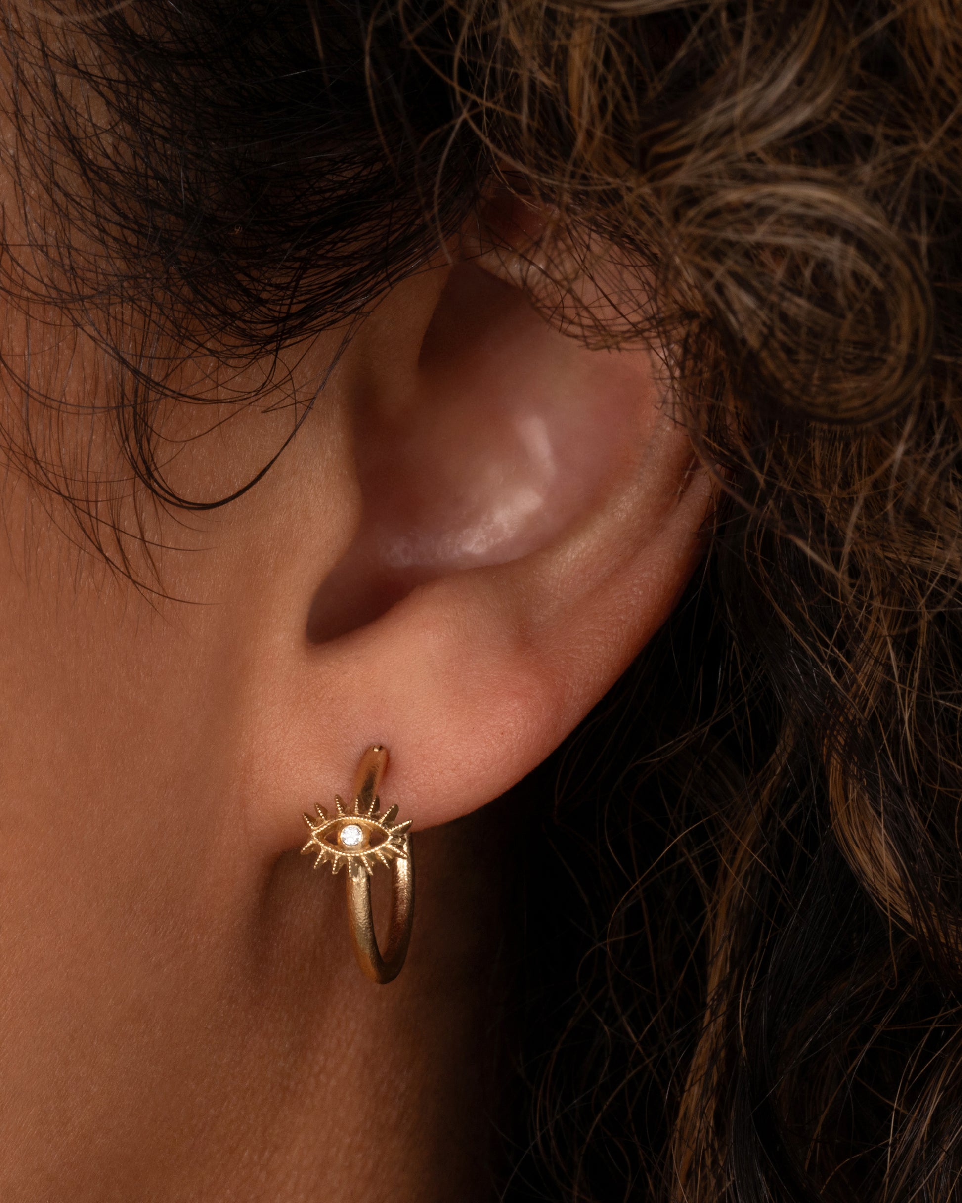 A yellow gold hoop earring with a diamond studded eye with dramatic lashes. Shown from the front on a person.