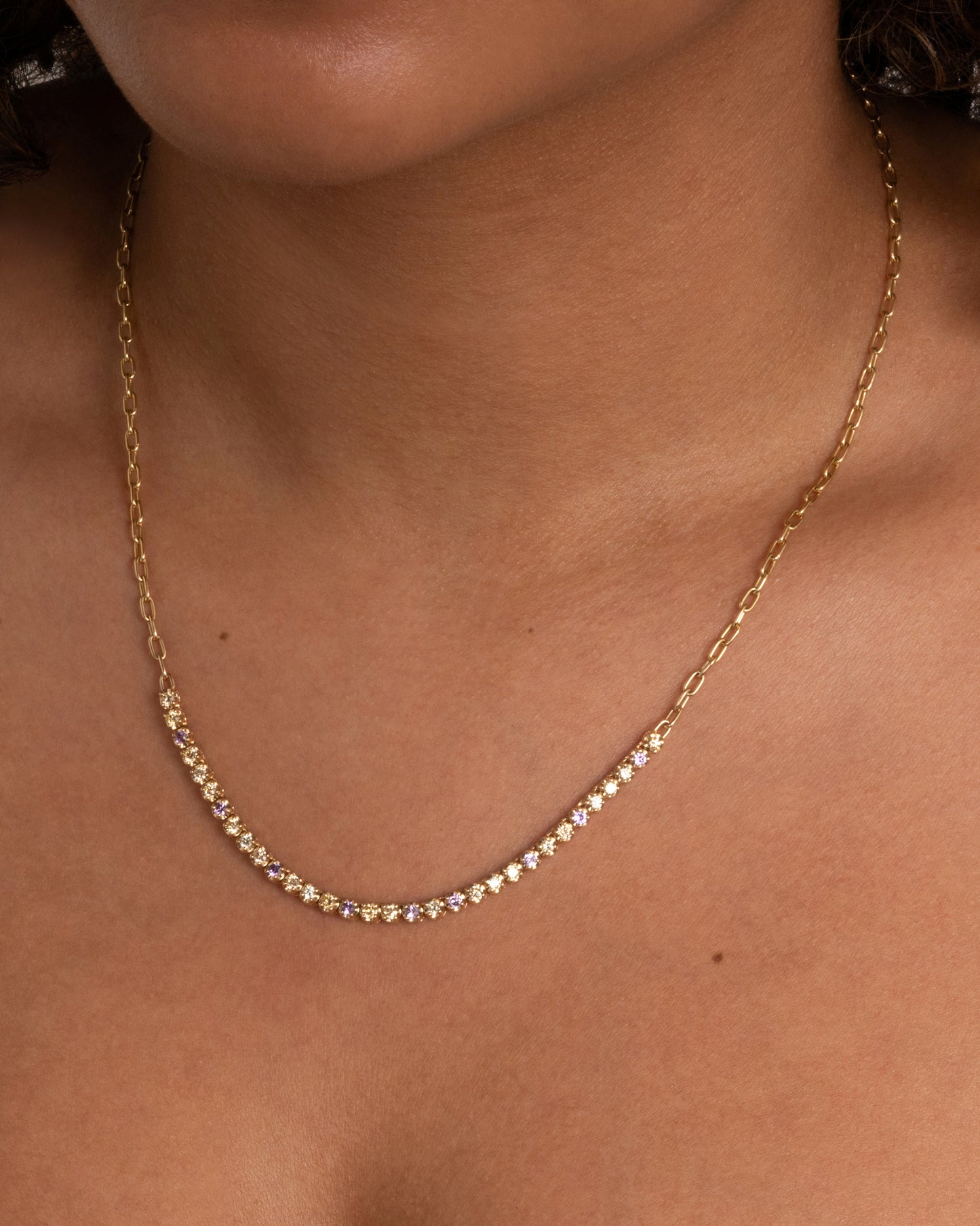 A yellow gold cable chain necklace with peach and yellow diamonds and purple sapphires in a 'partial tennis' setting. Shown from the front on a person.