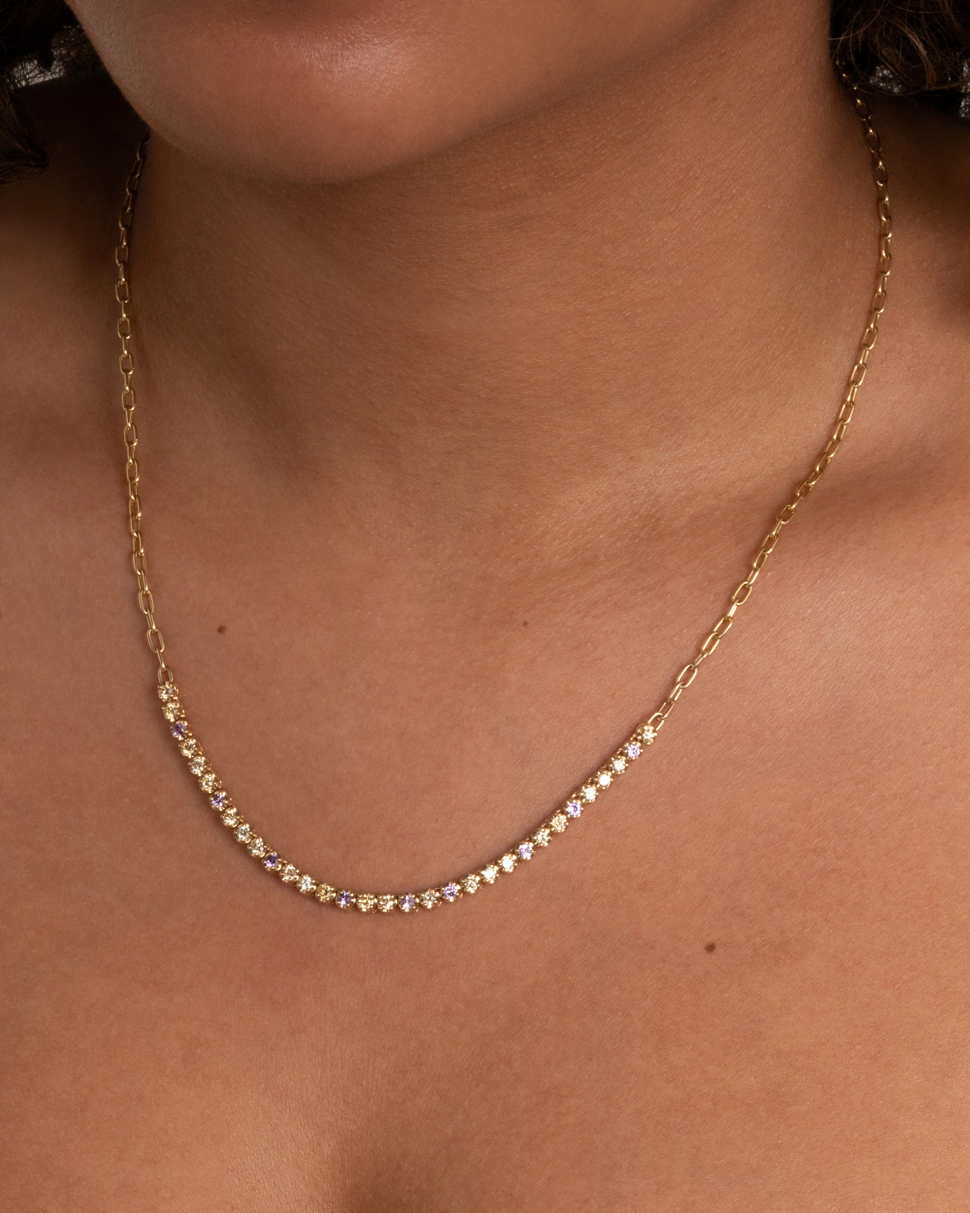 A yellow gold cable chain necklace with peach and yellow diamonds and purple sapphires in a 'partial tennis' setting. Shown from the front on a person.