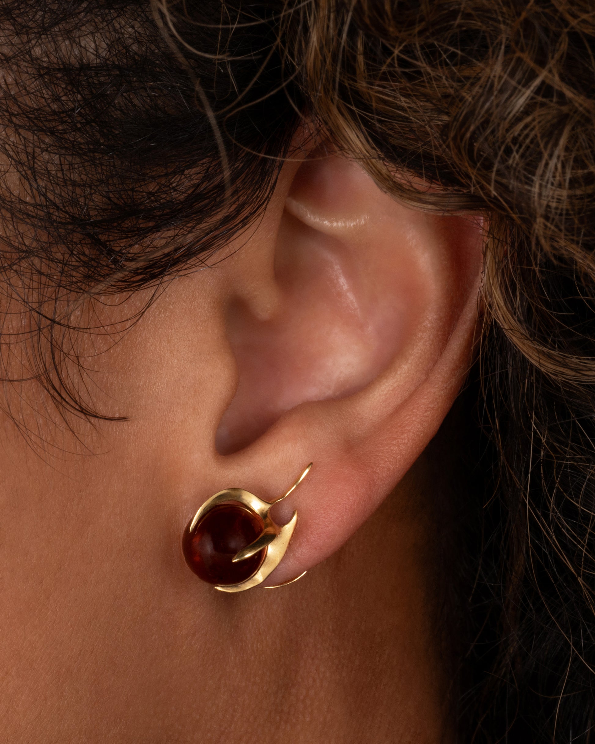 A yellow gold stud earring with a claw setting cradling a tourmaline sphere. Shown from the front on a person.