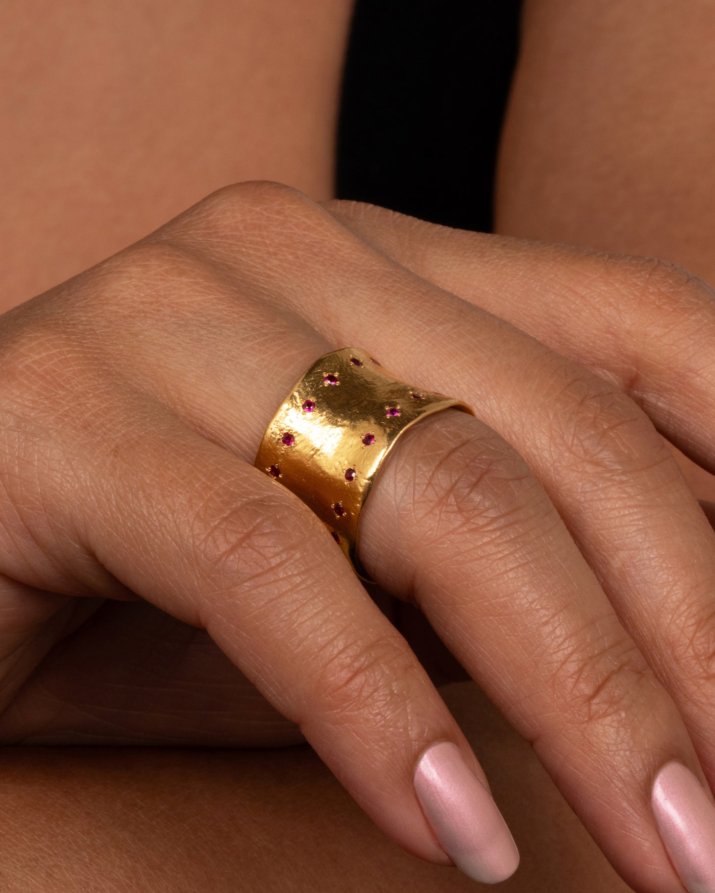 A slightly concave 22k gold band lined with thirty two rubies shown on a hand