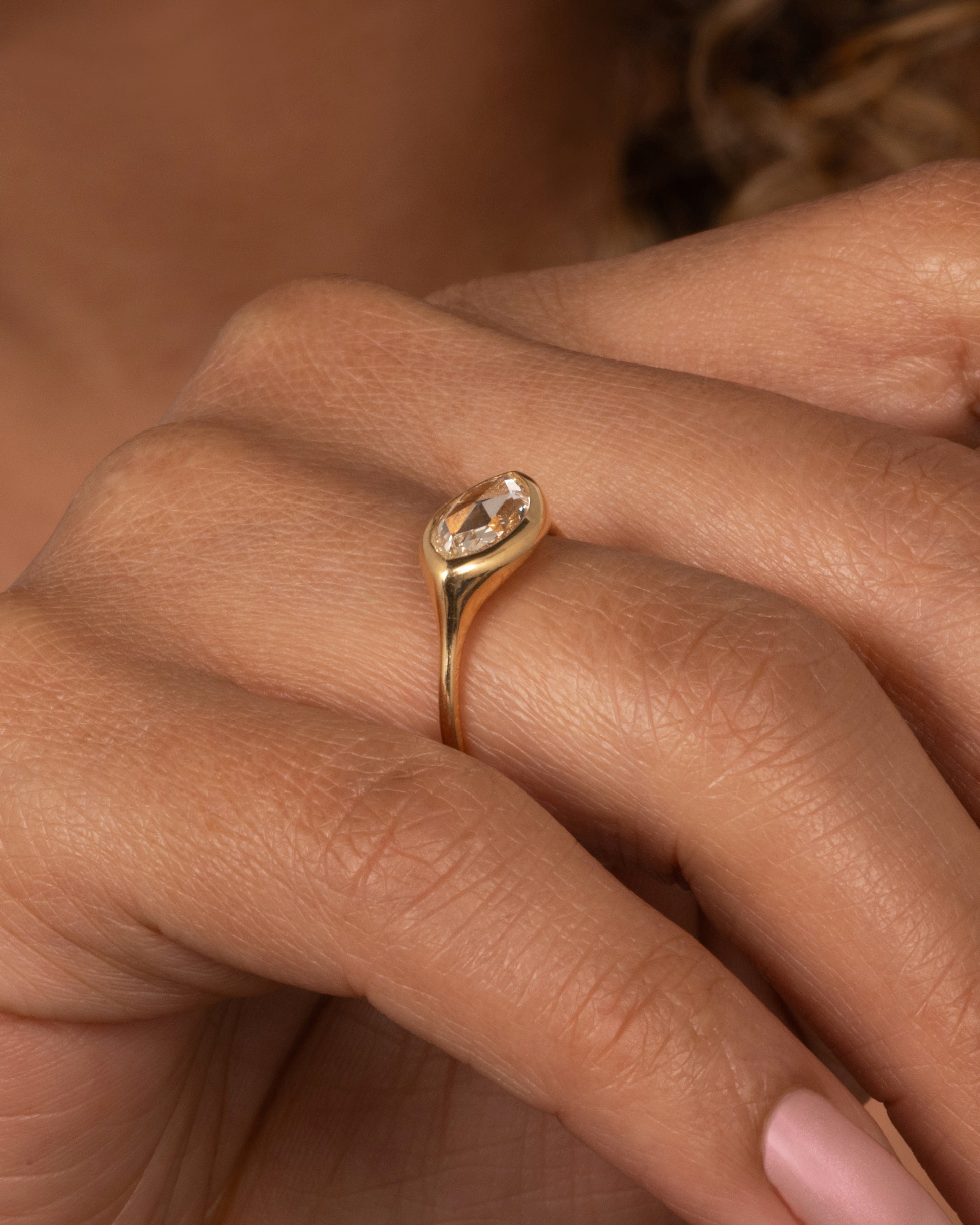 A yellow gold ring with a horizontal rose cut marquise diamond. Shown on a finger.