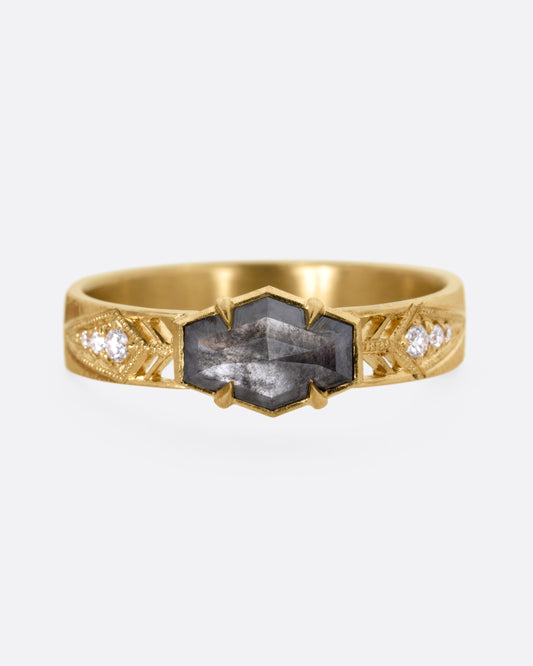 A yellow gold ring with a hexagonal black diamond, white diamond accents, and cutouts, shown from the front. 