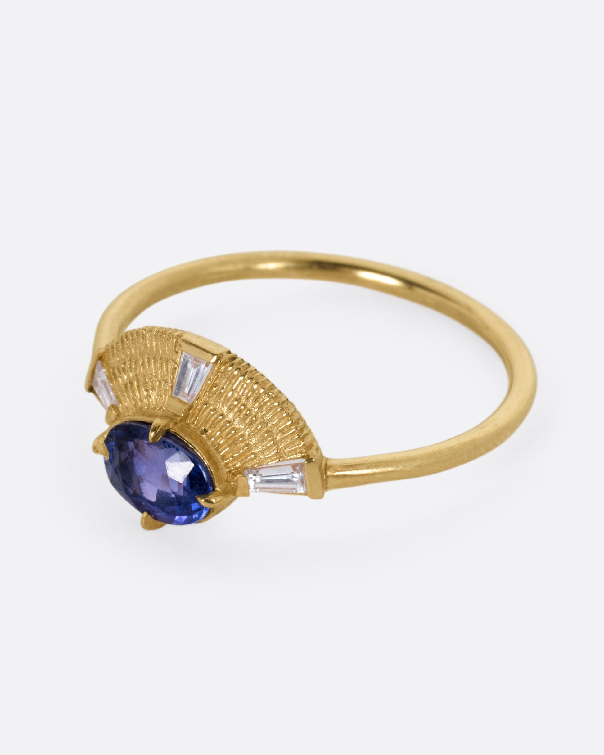 A yellow gold ring with a purple sapphire and three baguette diamonds, shown from the side.