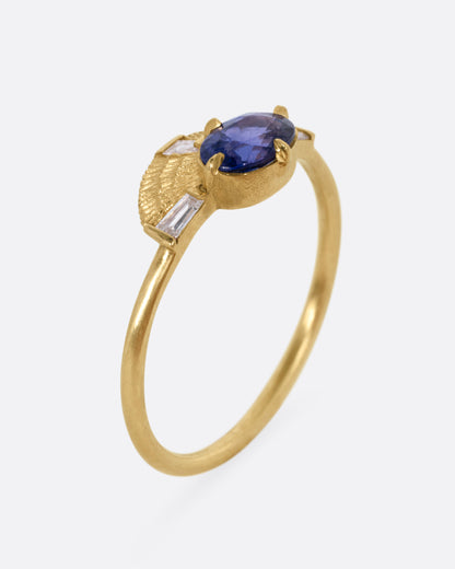 A yellow gold ring with a purple sapphire and three baguette diamonds, shown from the side standing up.