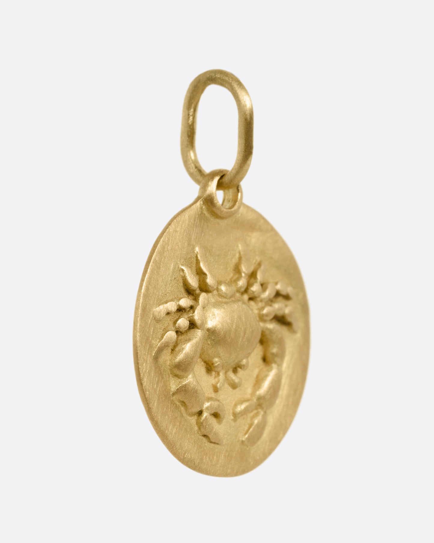 A circular yellow gold Cancer pendant with a crab on its front, shown from the side.
