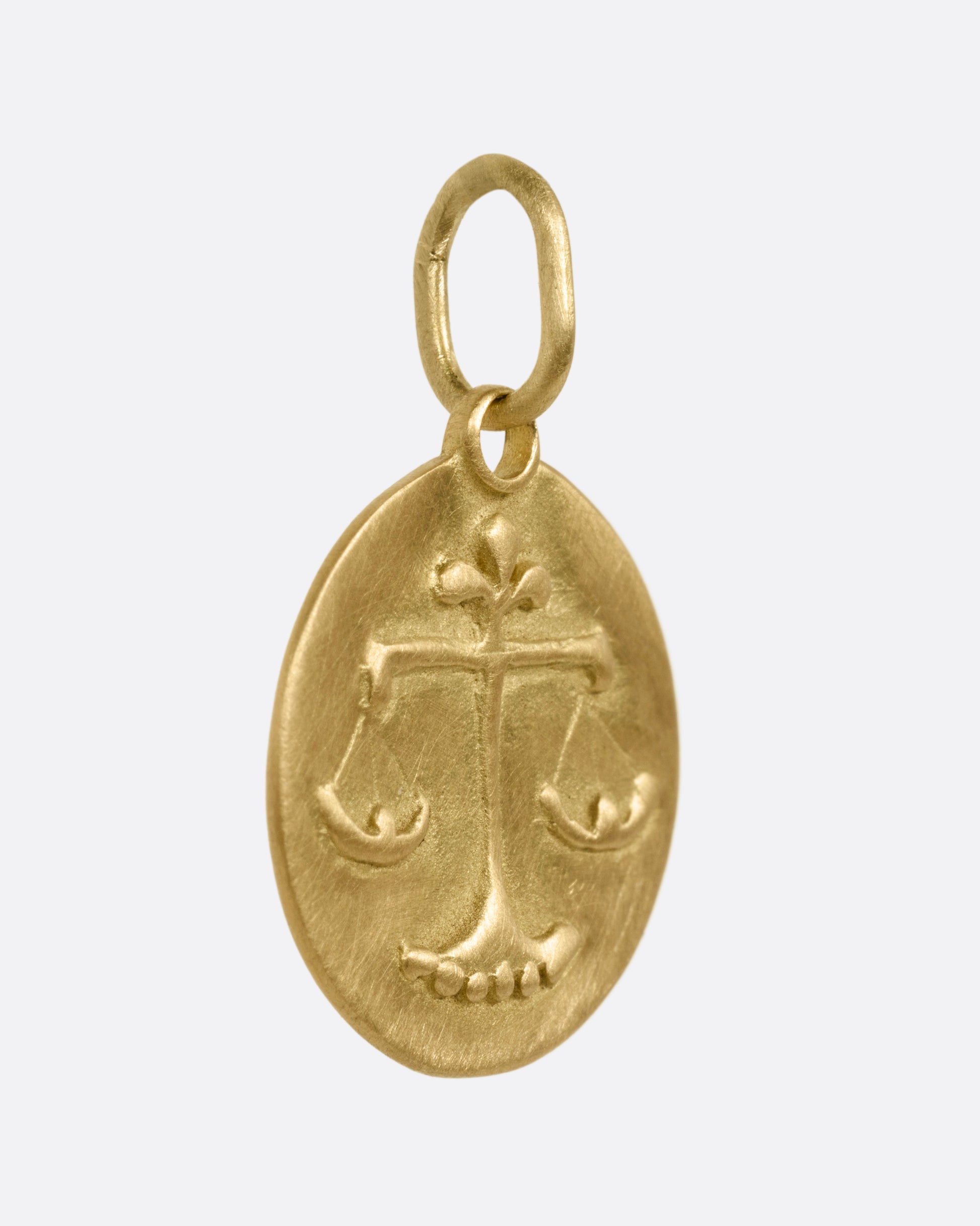 A circular yellow gold Libra pendant with the scales of balance, shown from the side.