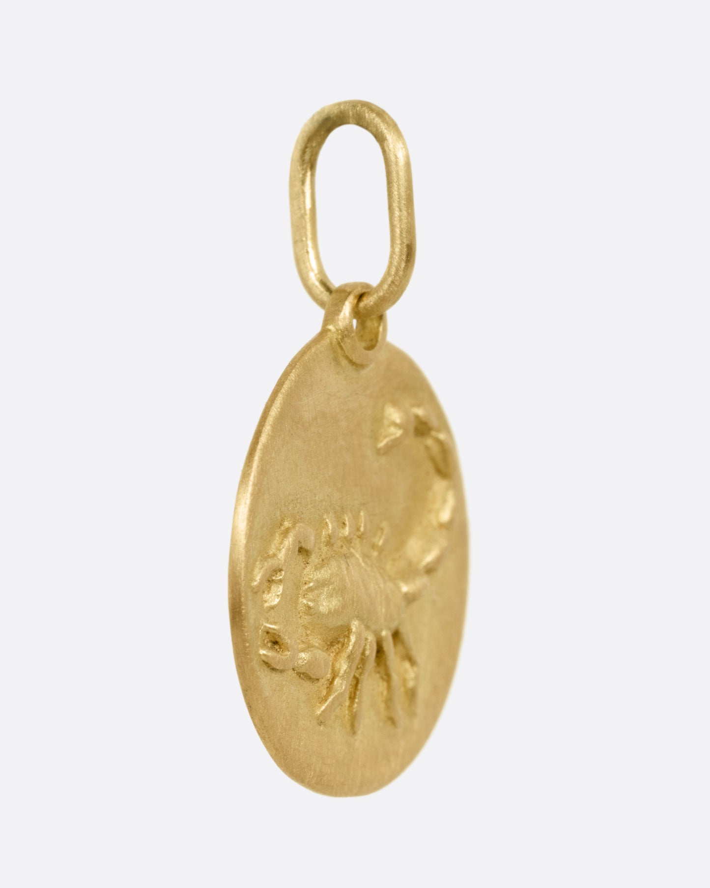 A circular yellow gold Scorpio pendant with a scorpion on its front, shown from the side.
