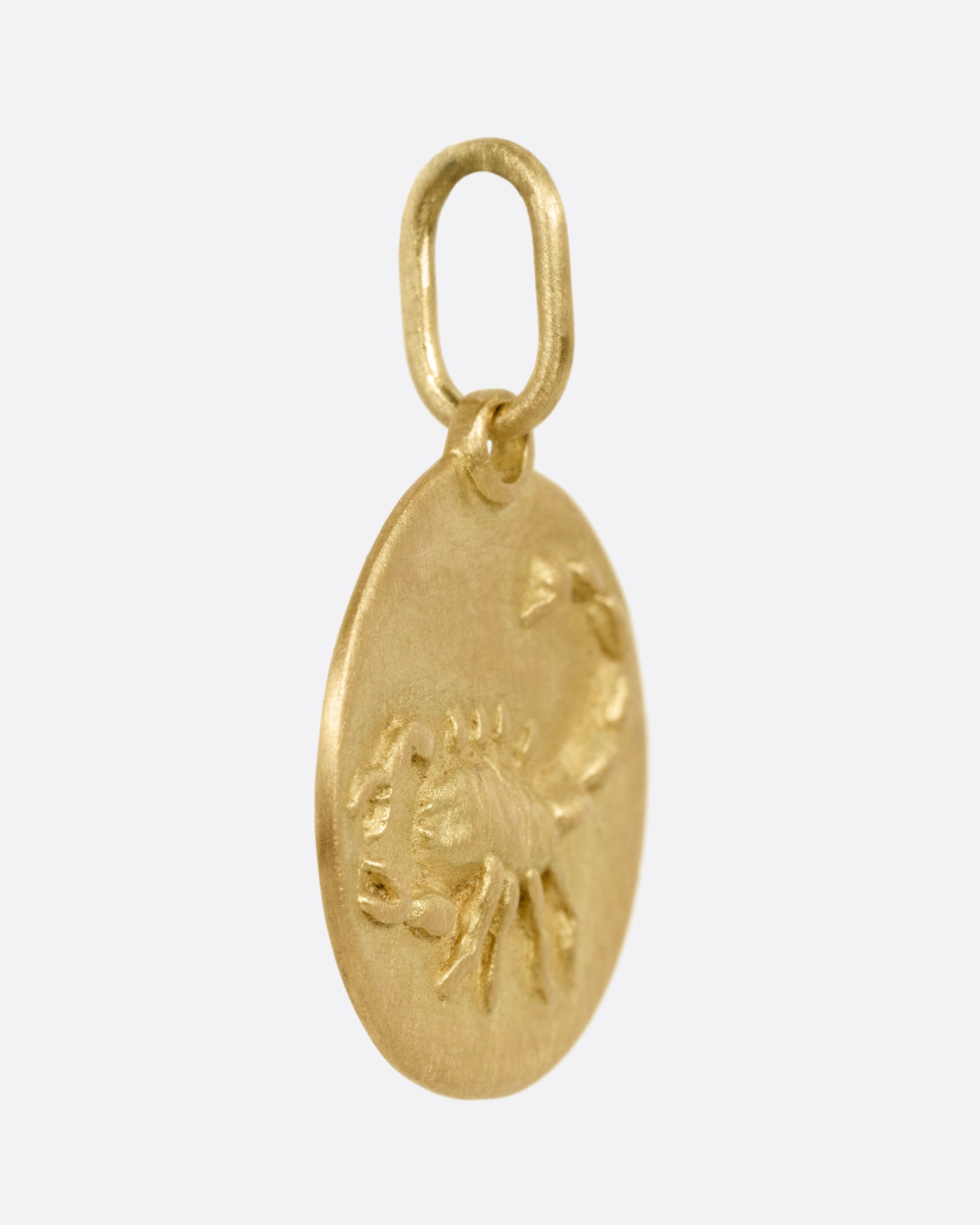 A circular yellow gold Scorpio pendant with a scorpion on its front, shown from the side.