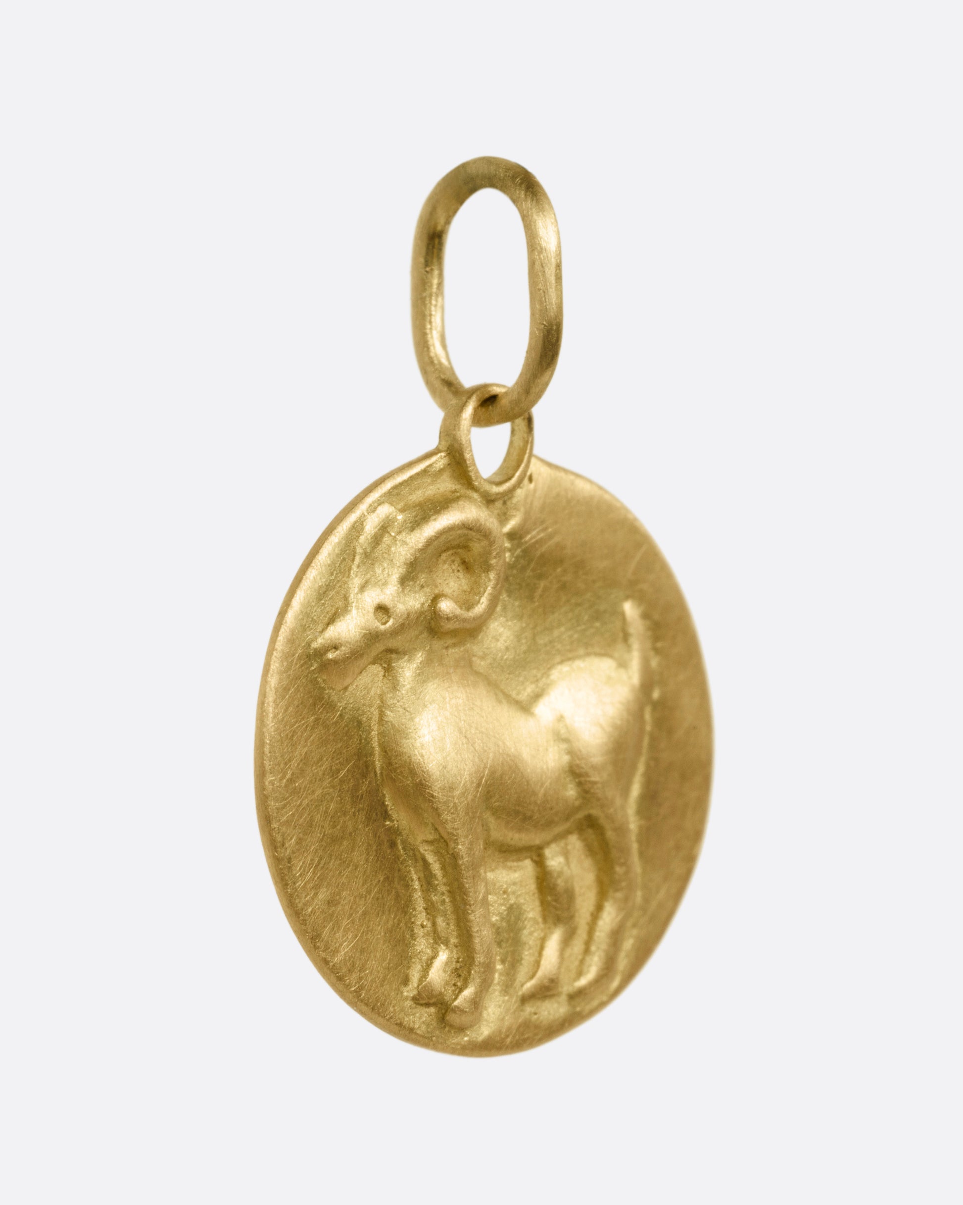 A yellow gold circular Aries pendant with a ram, shown from the side.