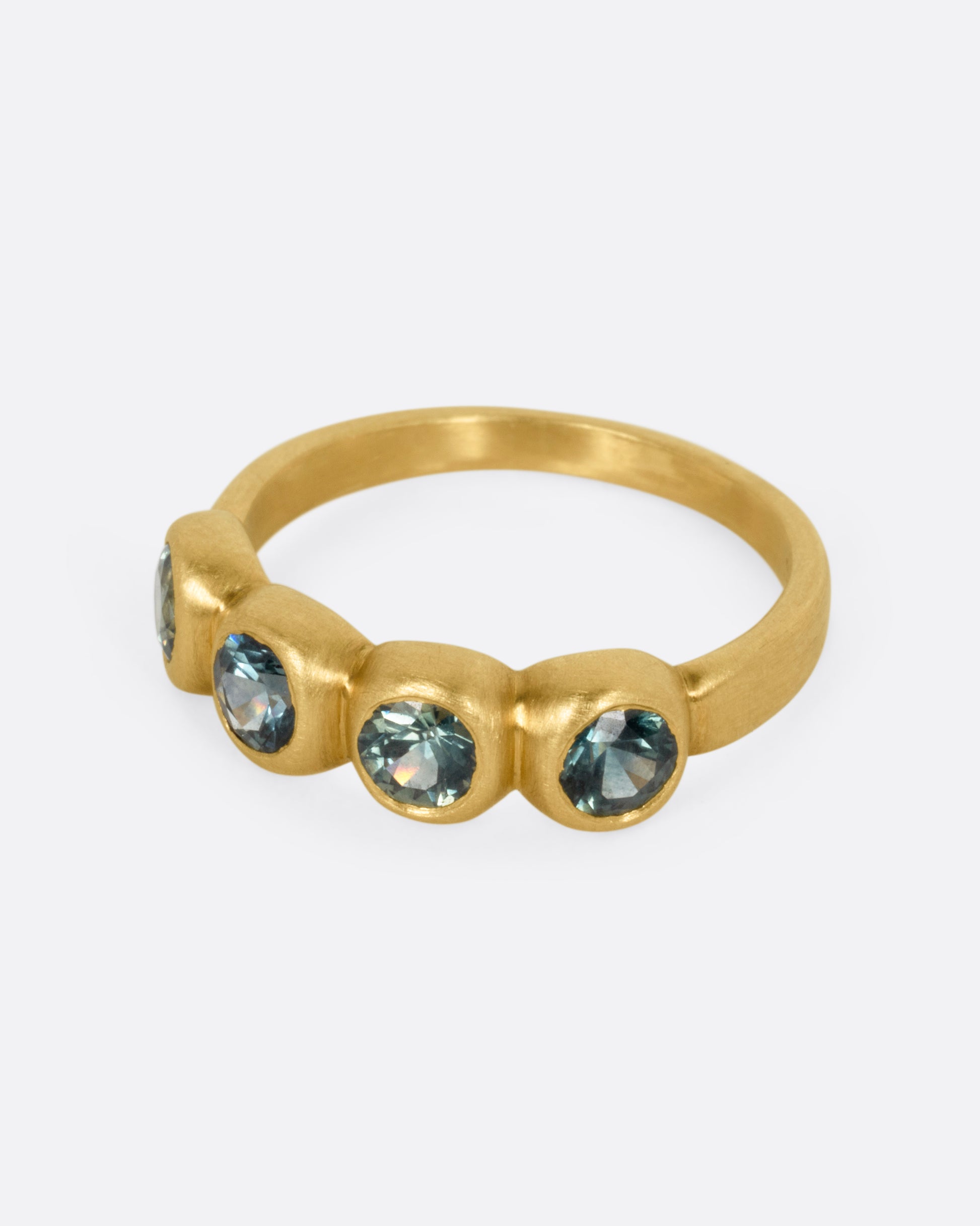 A yellow gold ring with four bezel set green sapphires, shown from the side.