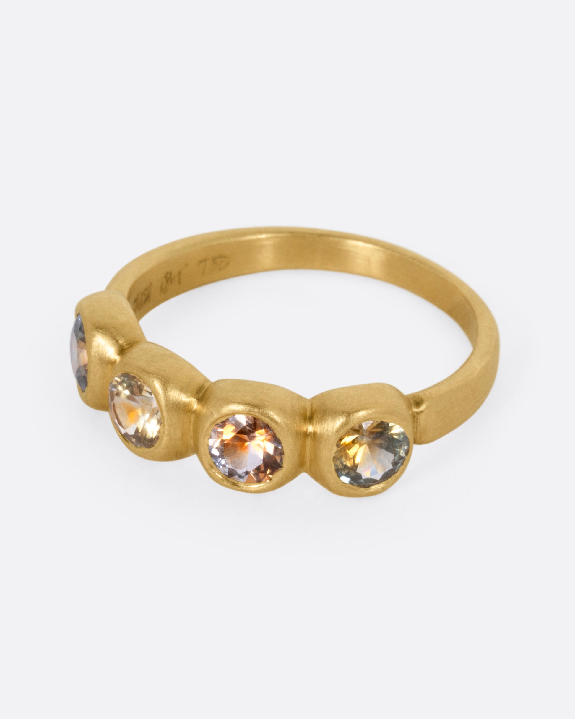 A yellow gold ring with four bezel set kaleidoscope sapphires, shown from the side.