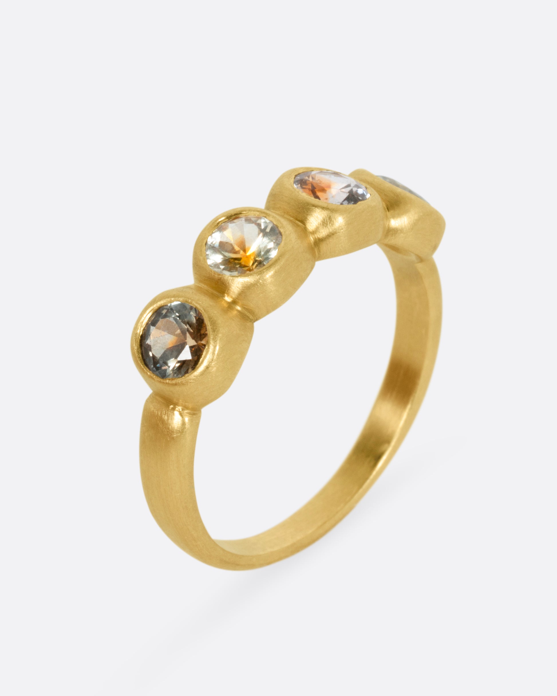 A yellow gold ring with four bezel set kaleidoscope sapphires, shown from the side standing up.