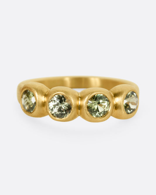 A yellow gold ring with four bezel set green sapphires, shown from the front.