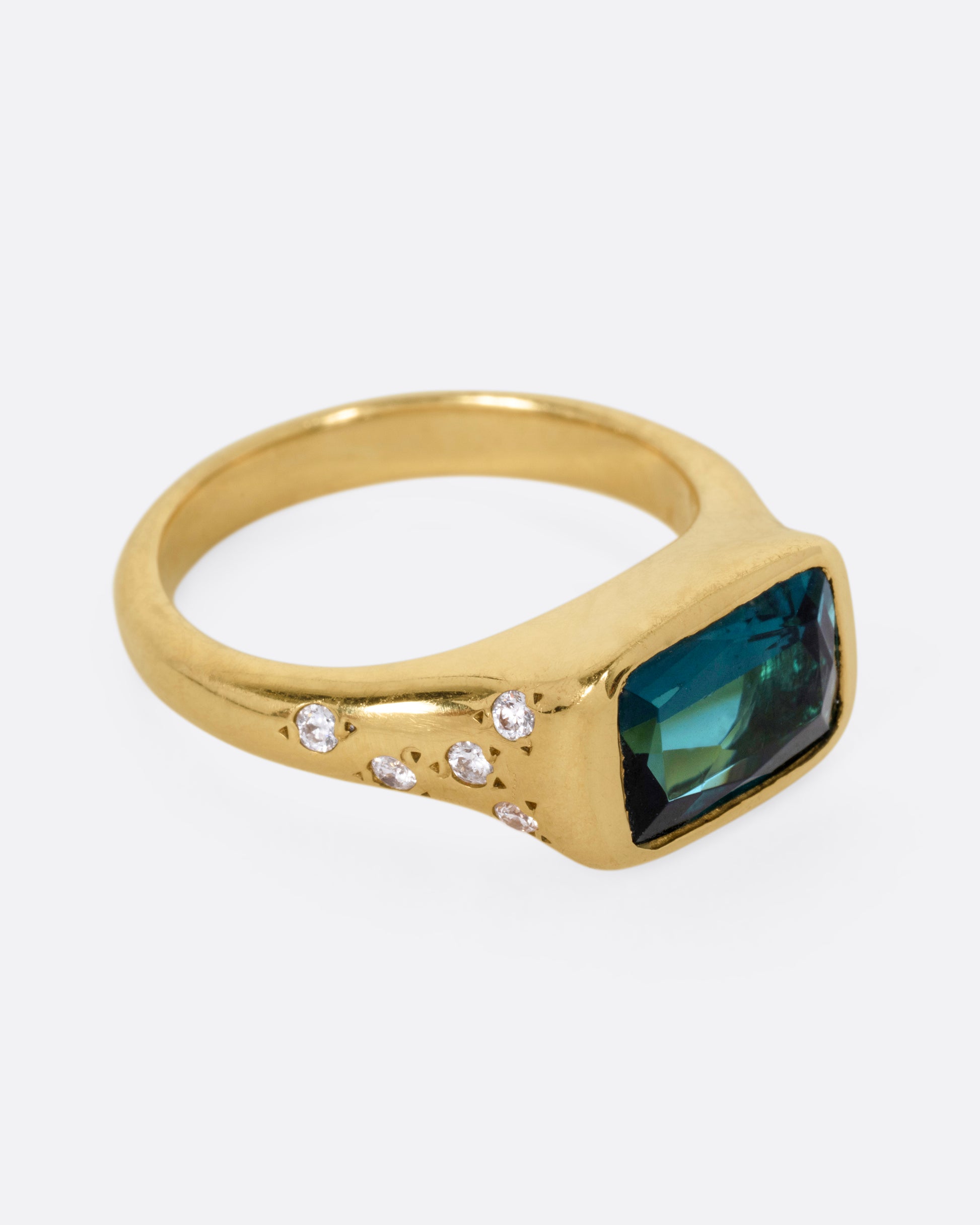 A yellow gold ring with a rectangular green tourmaline at the center and diamonds on either shoulder. Shown from the side.