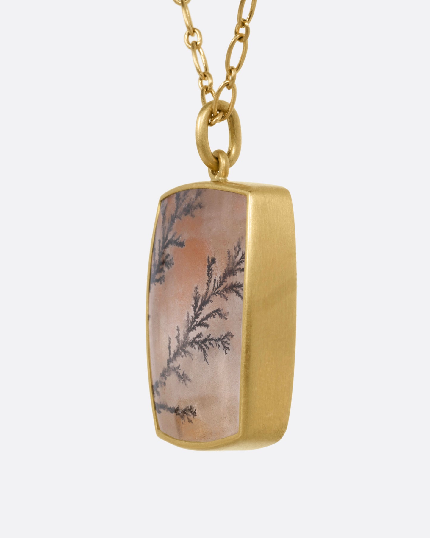 A yellow gold dendritic quartz pendant hanging from an alternating oval chain. Shown from the side.