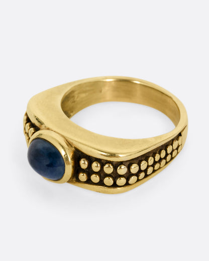 A yellow gold ring with a sapphire and raised circular pattern along the band, shown from the side.