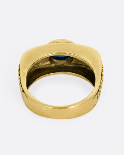 A yellow gold ring with a sapphire and raised circular pattern along the band, shown from the back.