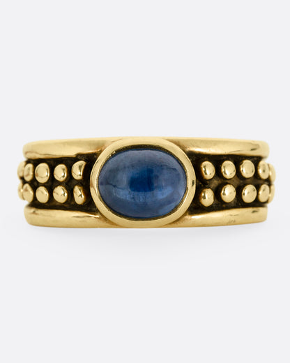 A yellow gold ring with a sapphire and raised circular pattern along the band, shown from the front.