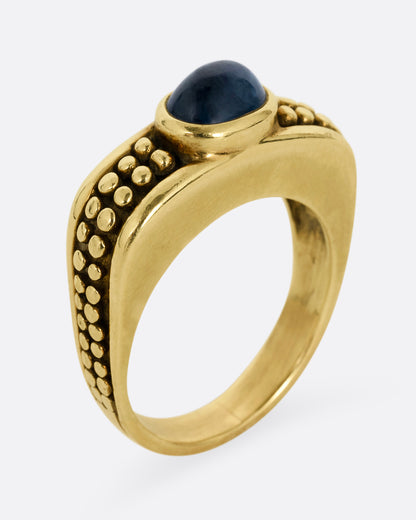 A yellow gold ring with a sapphire and raised circular pattern along the band, shown standing up from the side.