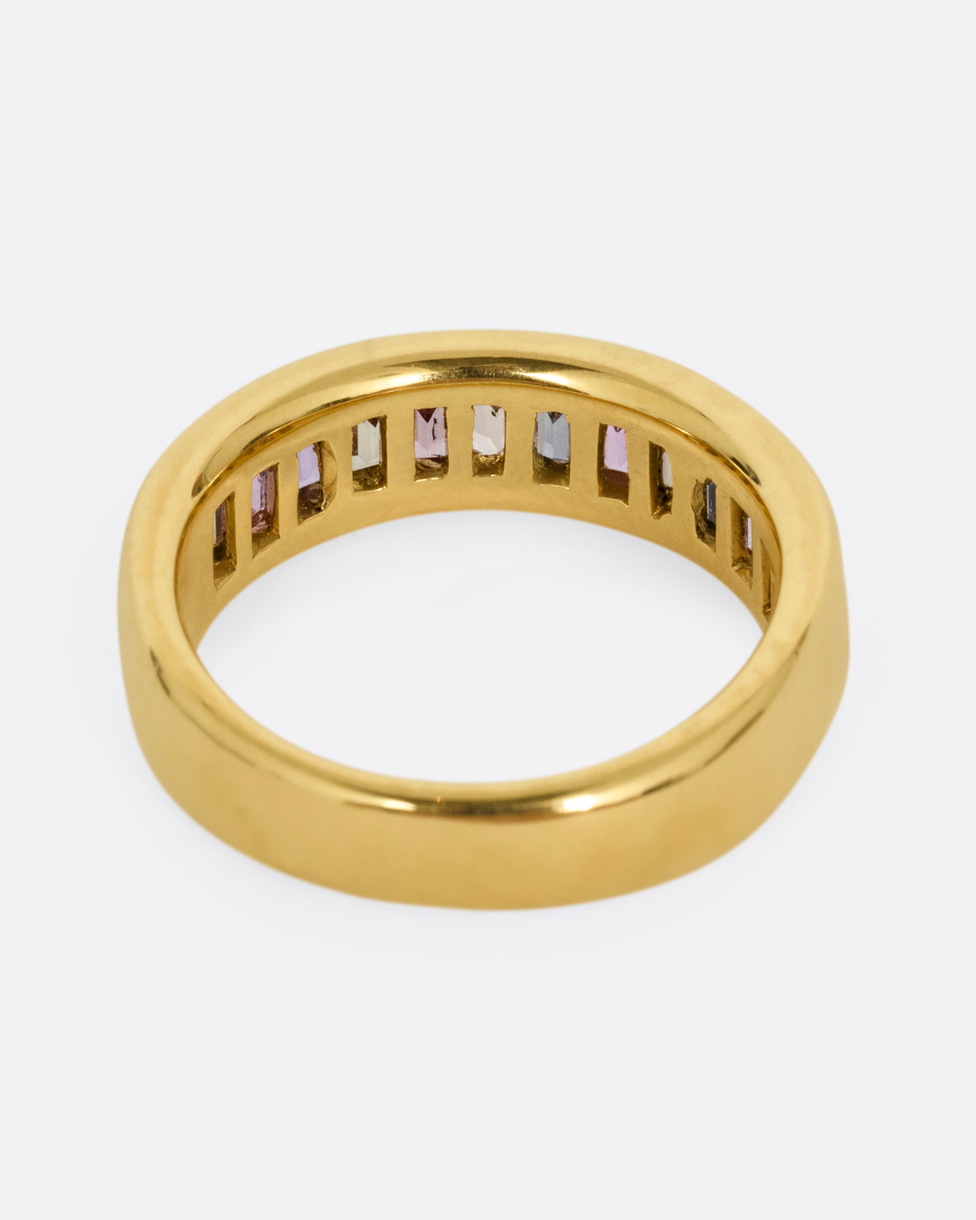 A yellow gold ring with channel set multicolored sapphires. Shown from the back.