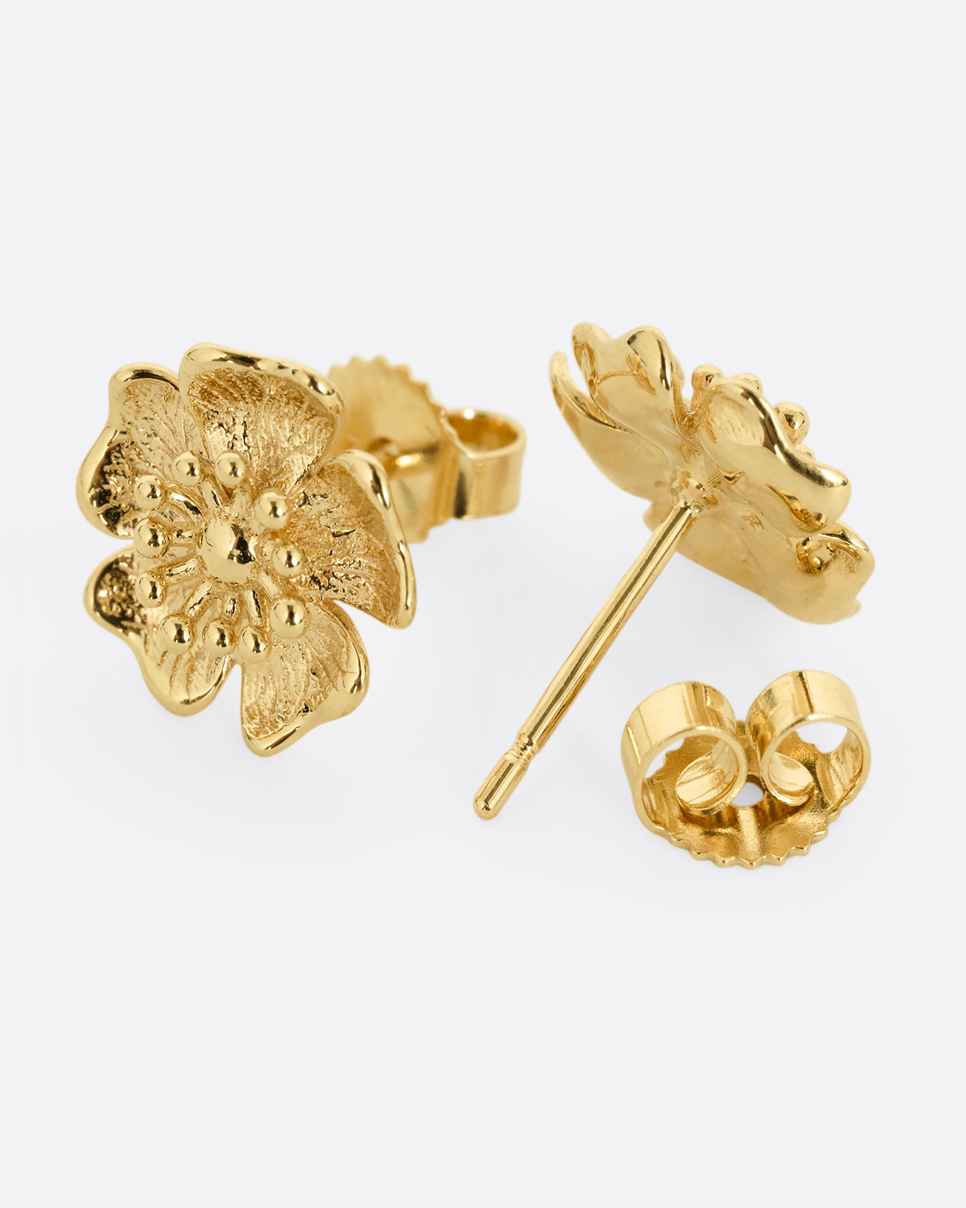 A pair of yellow gold flower stud earrings. One earring is shown from the front, the other is shown open from the back.