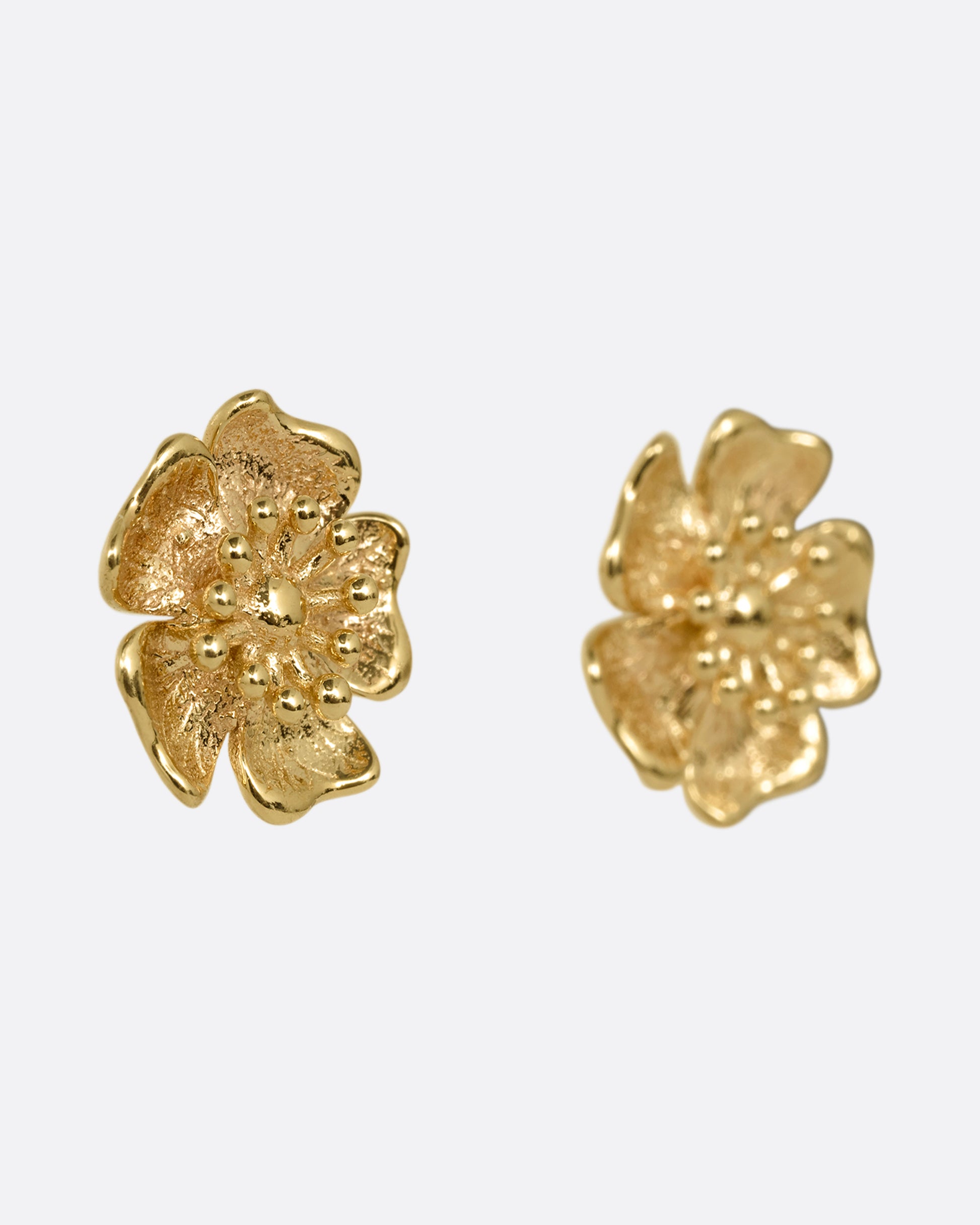 A pair of yellow gold flower stud earrings. Shown from the side.